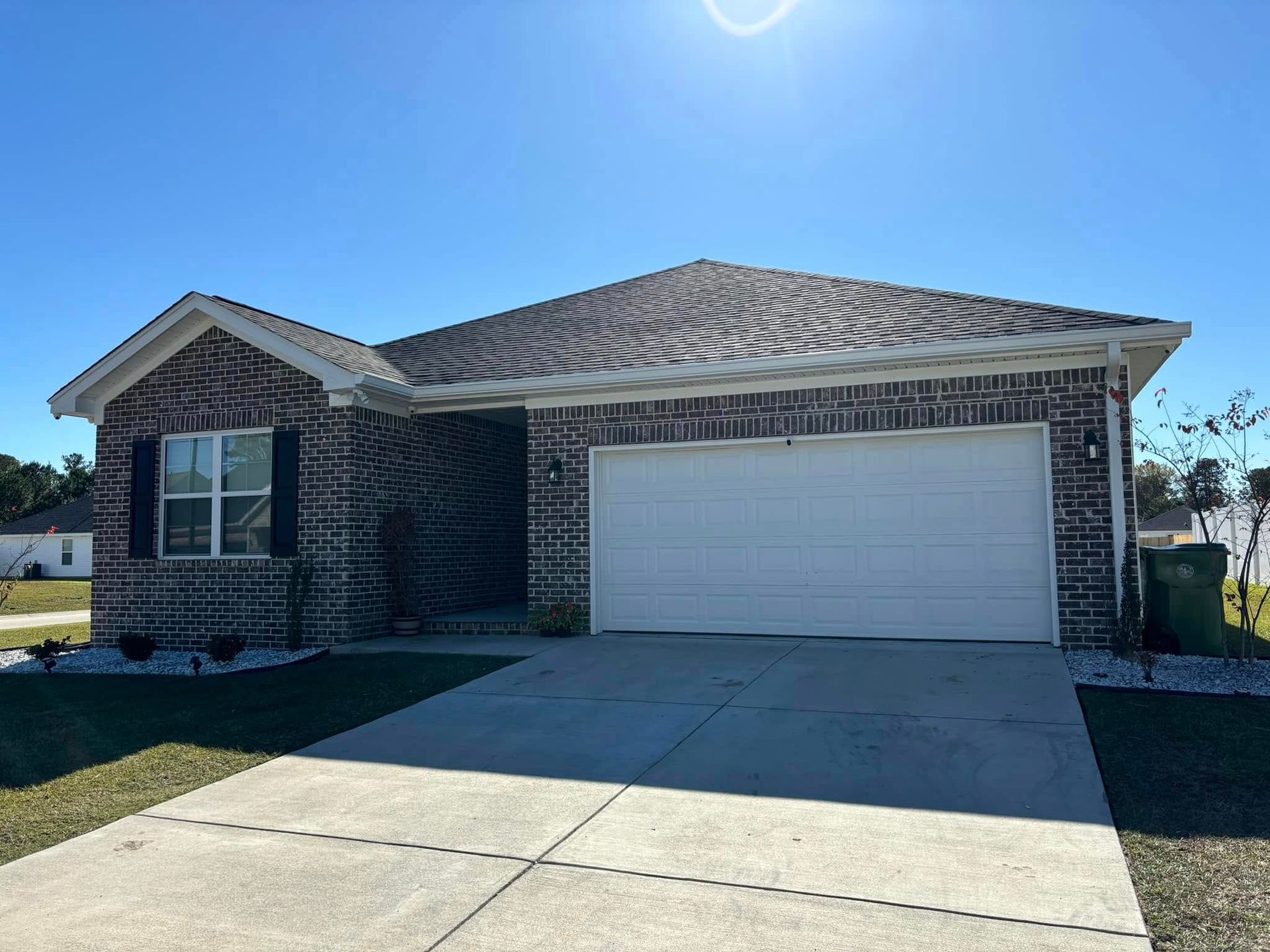 Single-story brick house with a white garage door and concrete driveway under a clear blue sky
