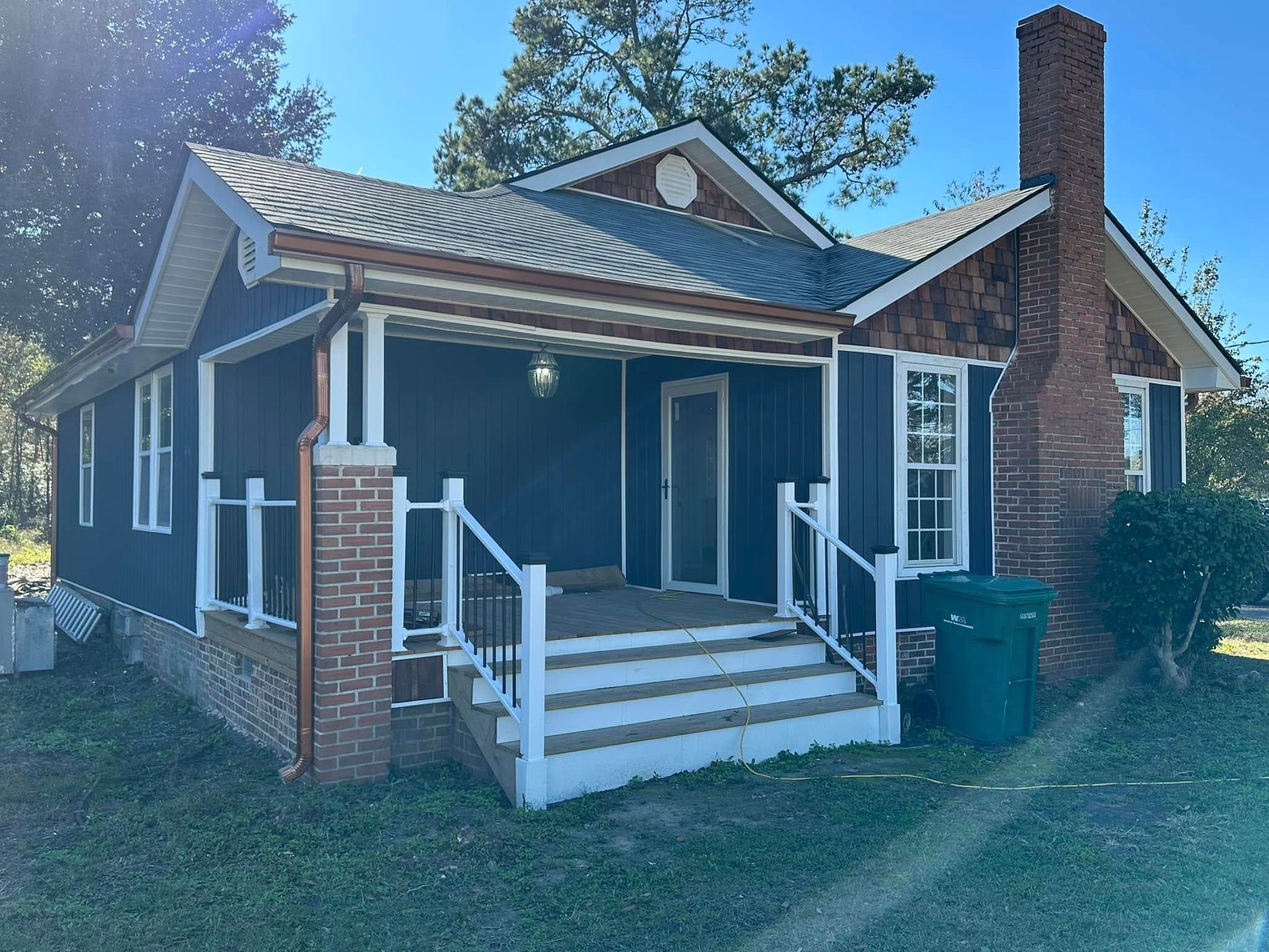 Small blue house with a front porch, white trim, brick chimney, and steps in a grassy yard
