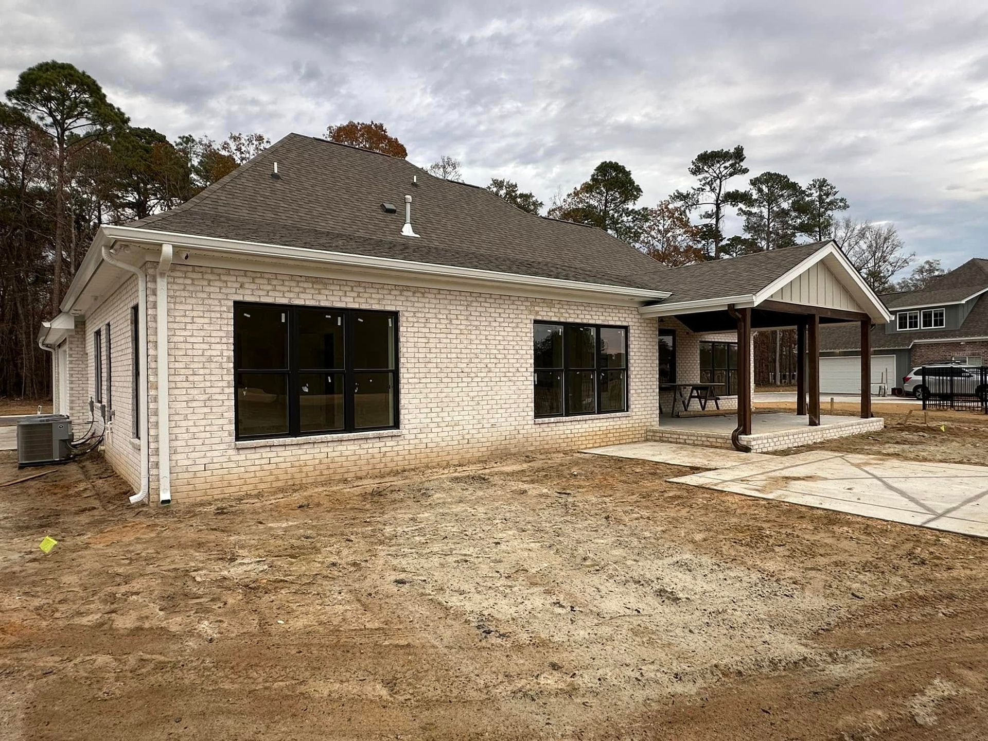 Single-story brick house under construction with dark windows and a covered patio, surrounded by bare dirt.