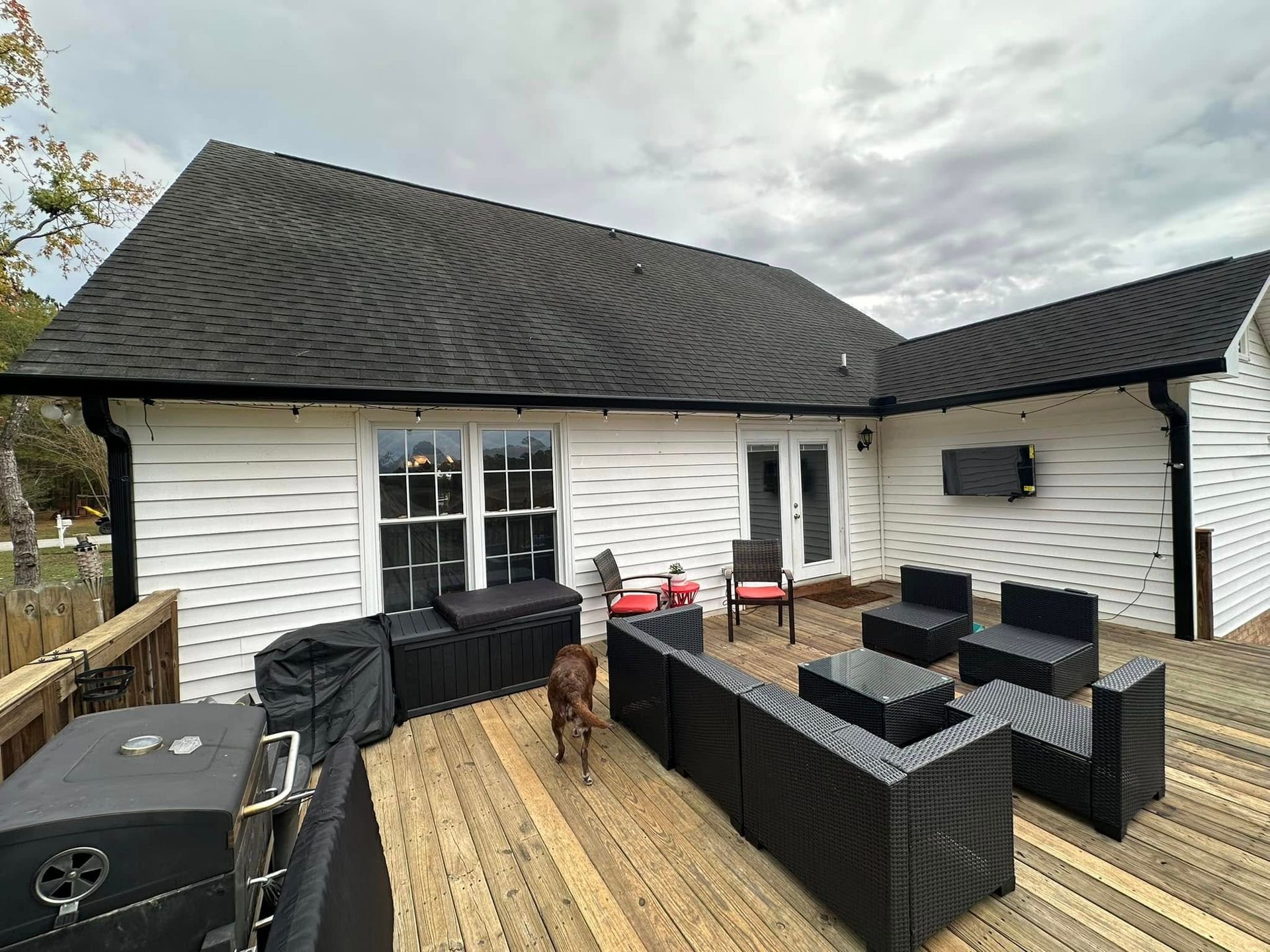 Back patio with black wicker furniture, a grill, and a dog on a wooden deck behind a white house