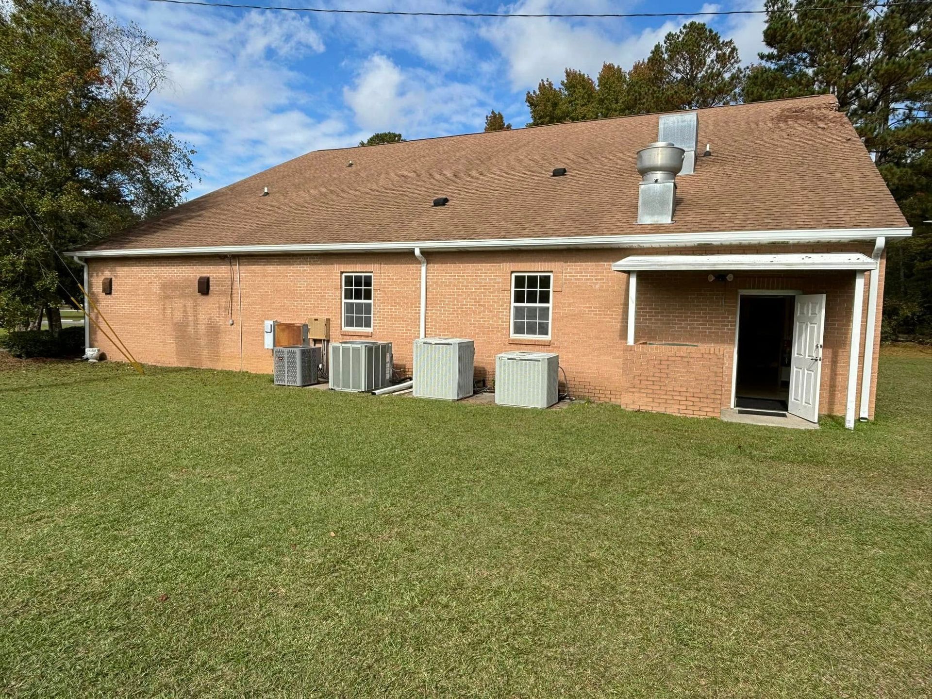 Brick house with a grassy yard and several outdoor HVAC units under a partly cloudy sky