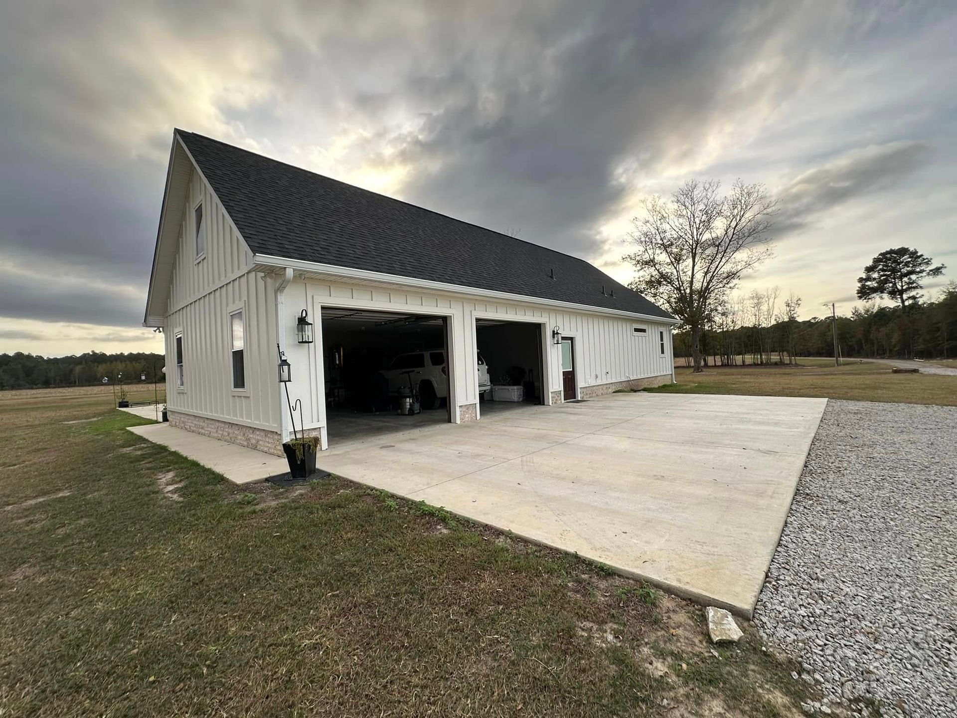 White detached garage with open bays and concrete driveway on a cloudy rural property