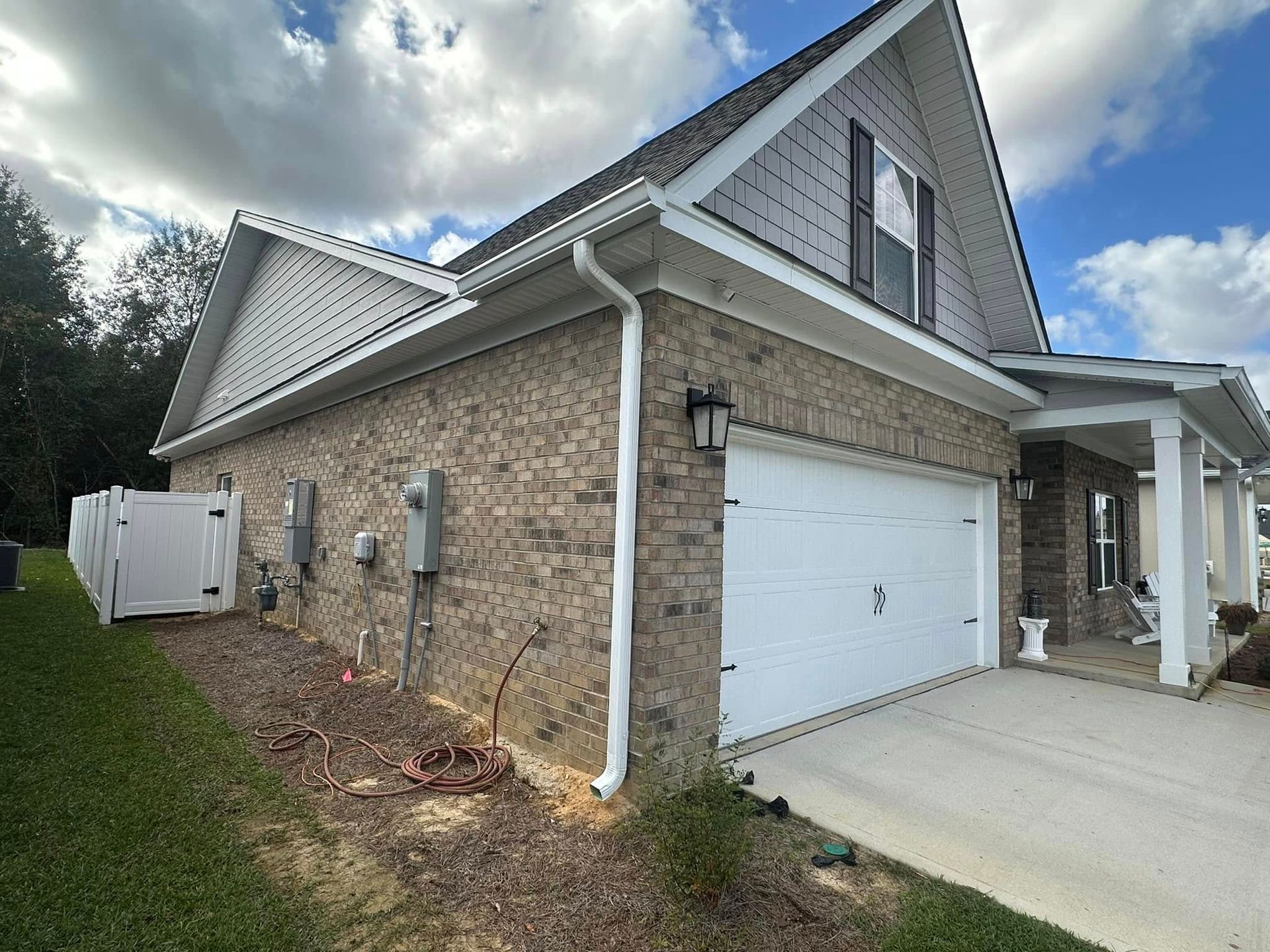 Suburban house exterior with brick siding, white garage door, and covered front porch under a cloudy sky