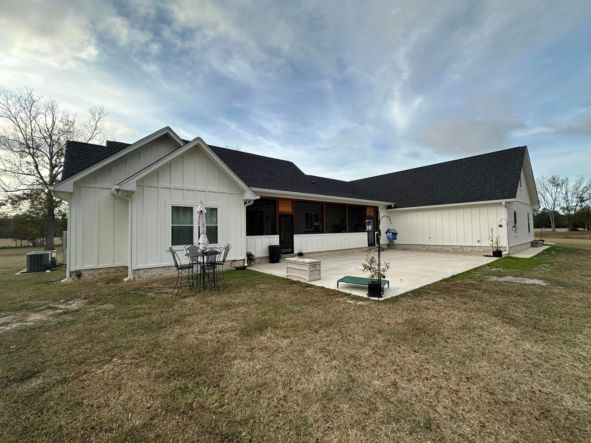 Single-story white house with dark roof, small patio, and grassy yard under a cloudy sky