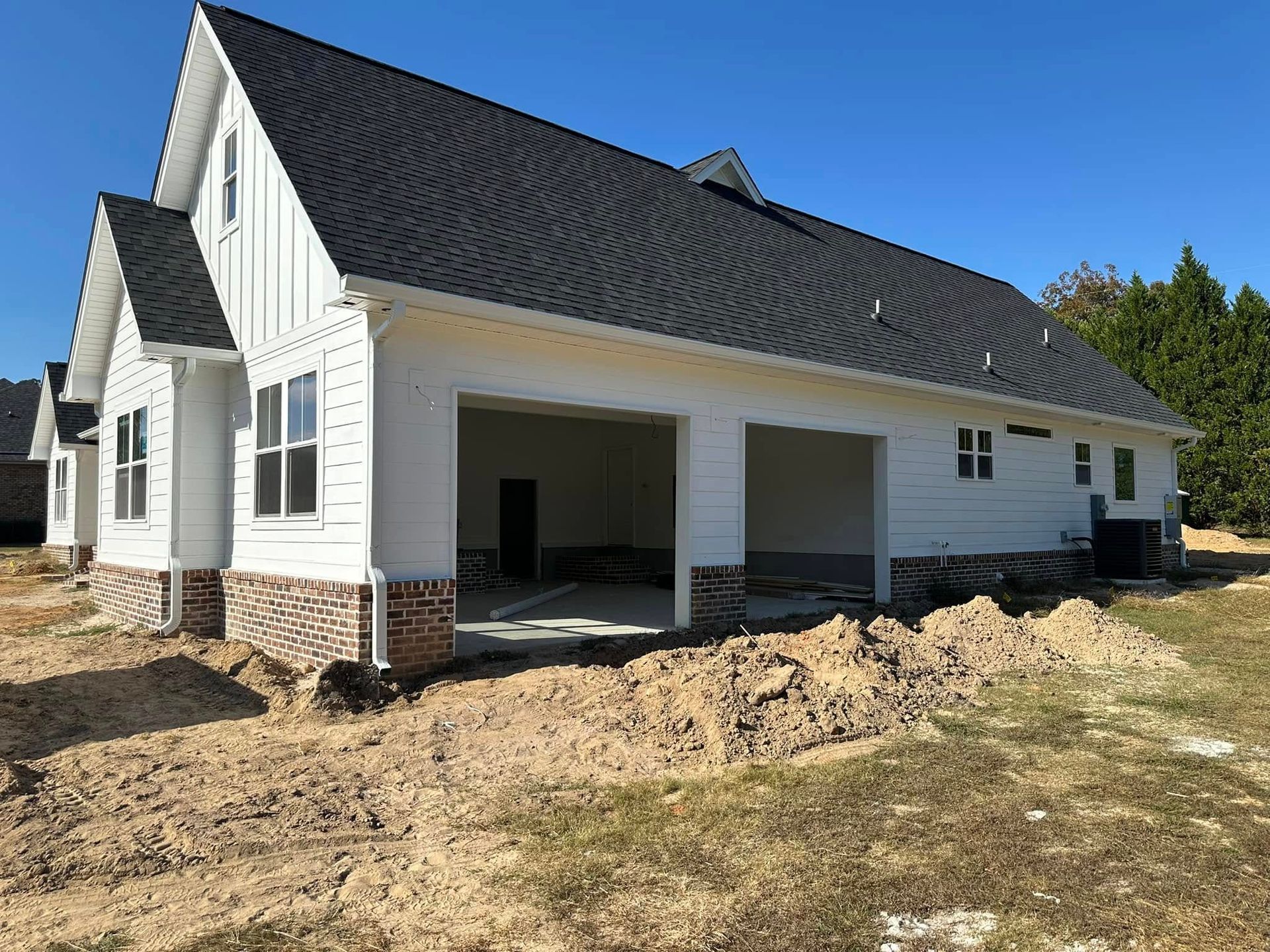 White house with dark roof and covered porch, surrounded by unfinished dirt yard under a clear blue sky