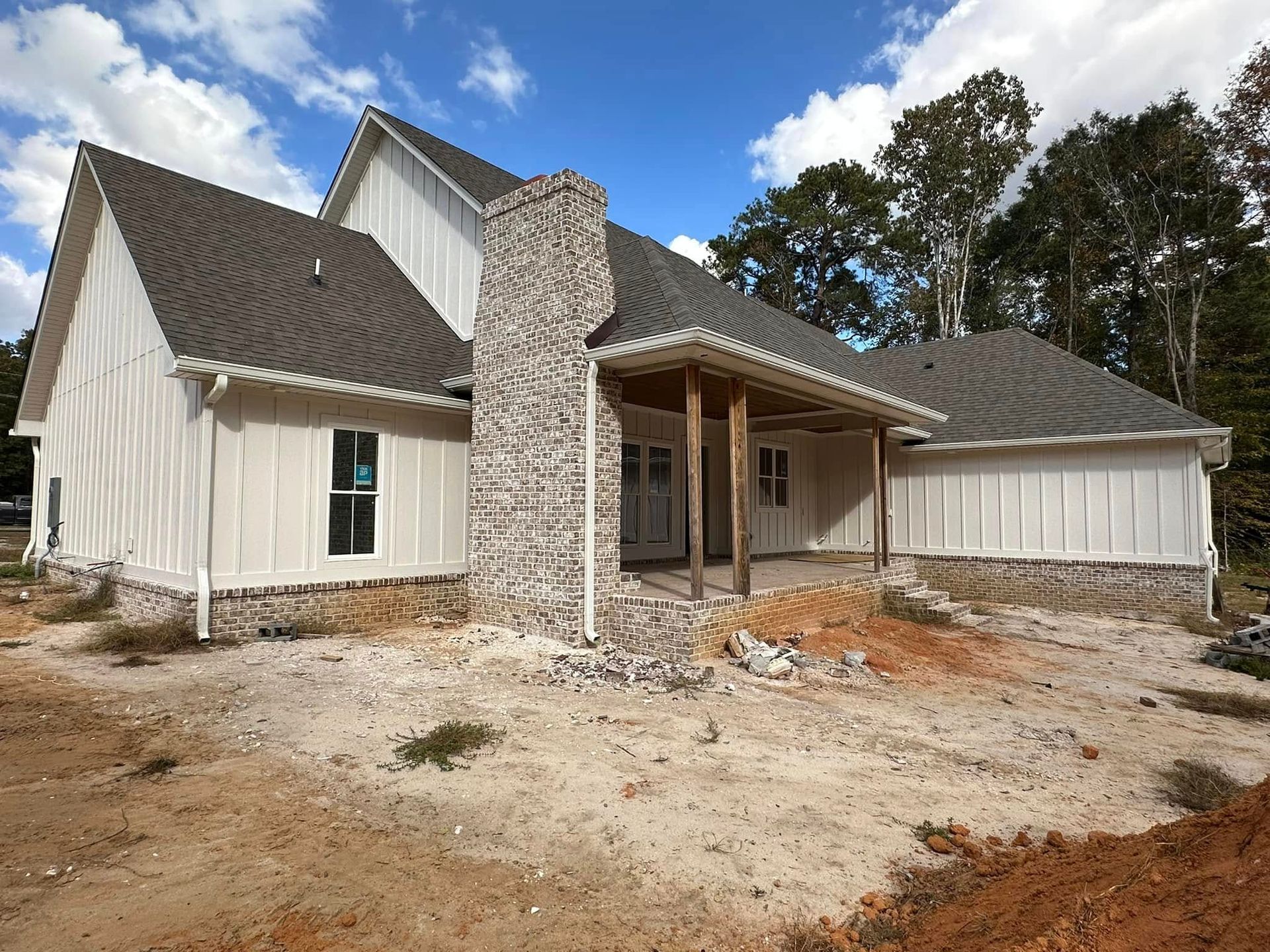 New white house with stone chimney and covered porch on a bare construction lot under a blue sky