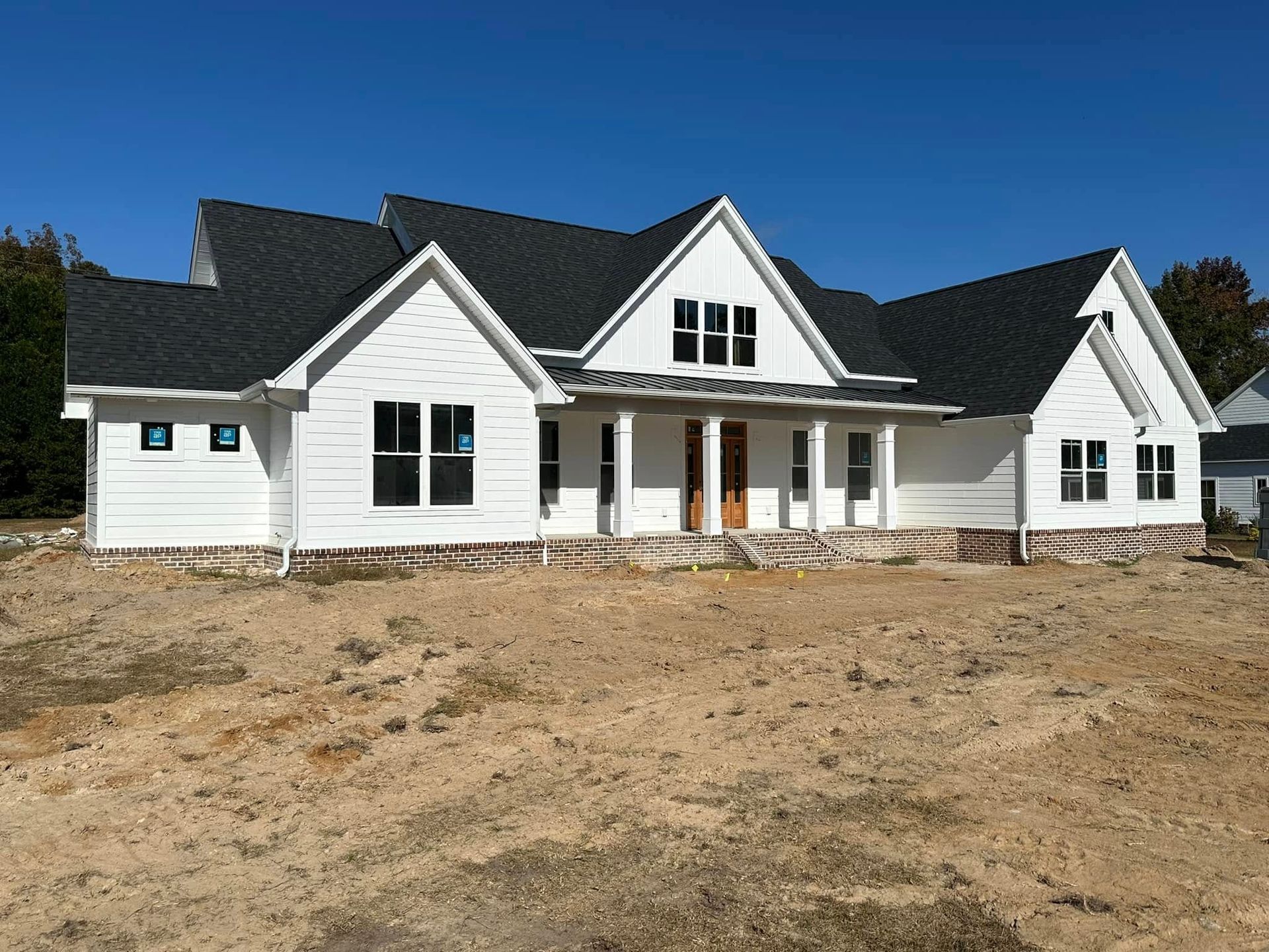 White house with black roof under construction on a bare lot under a clear blue sky