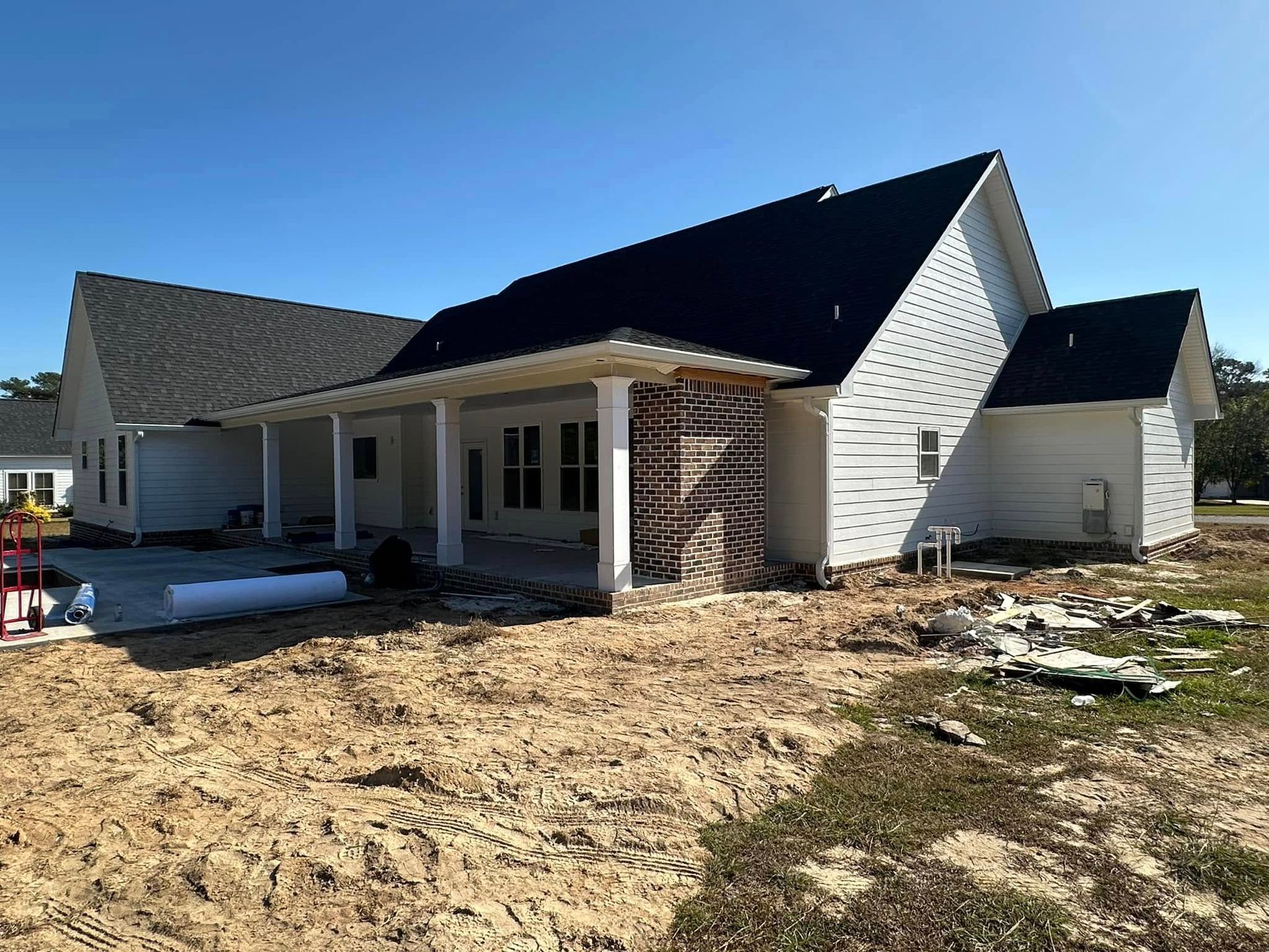 Partially built house with white siding, black roof, and bare dirt yard under a clear blue sky