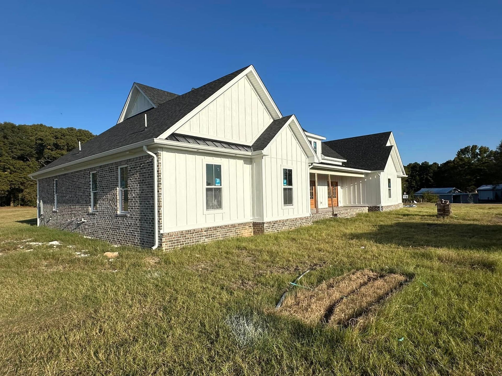 White farmhouse with gray roof in a grassy field under a clear blue sky