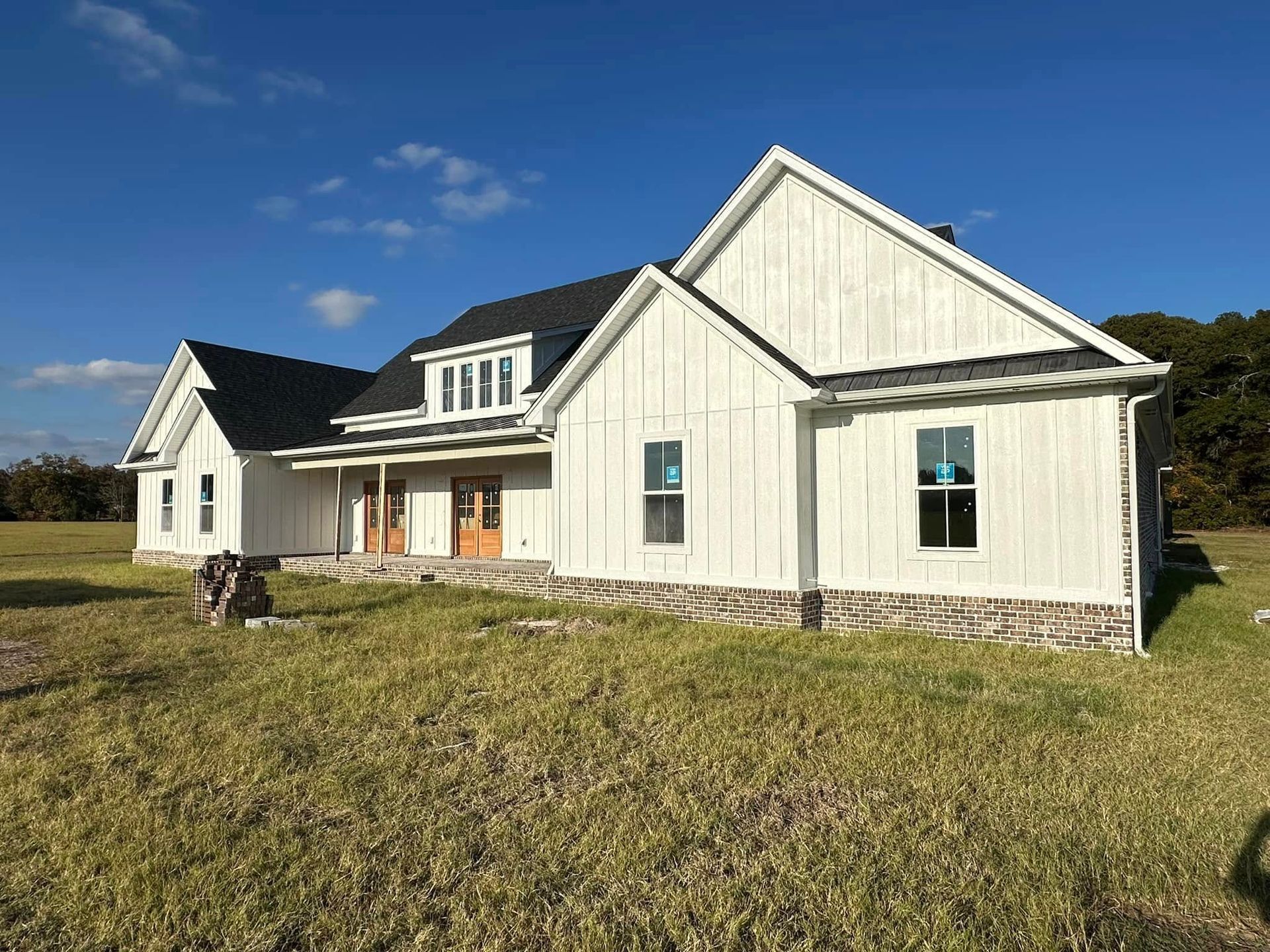 White farmhouse exterior with dark roof and front porch on a grassy lot under a blue sky