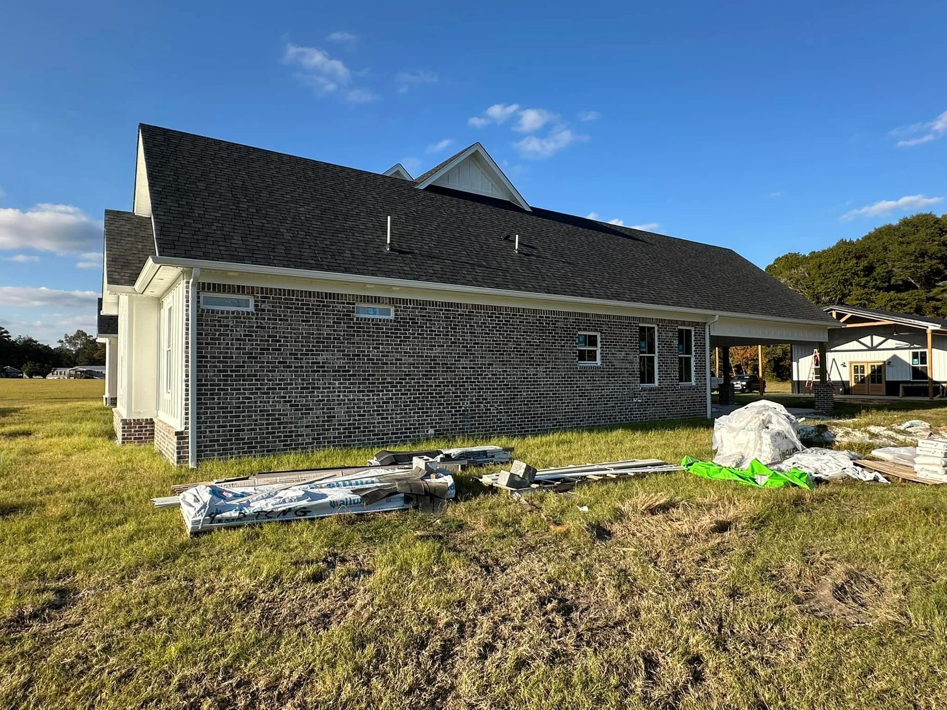 House under construction with dark siding and roof, materials on the ground, and blue sky overhead