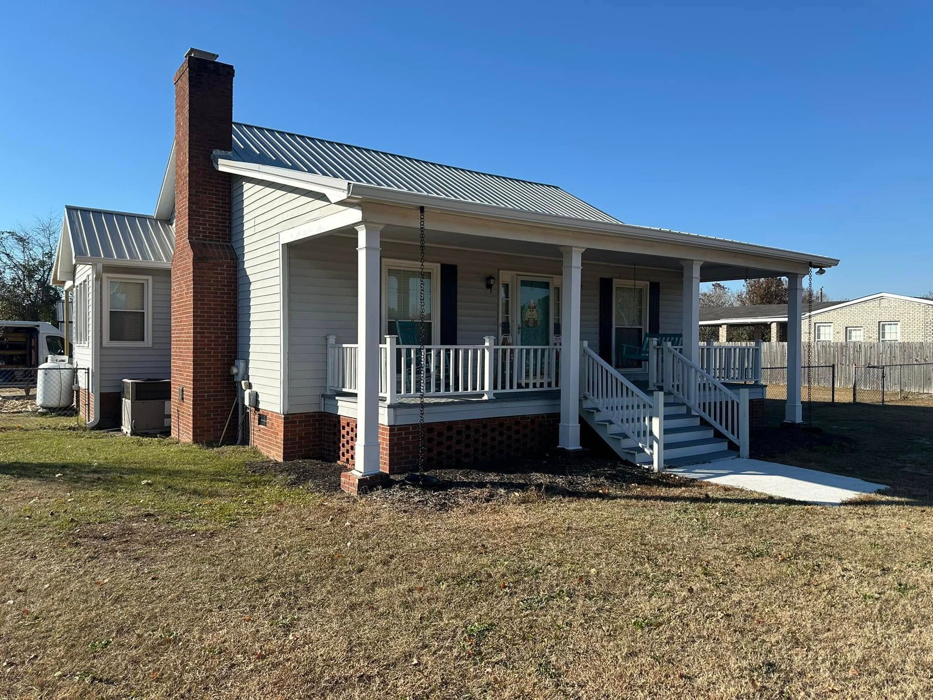 Small white house with a front porch, brick chimney, and ramp in a grassy yard