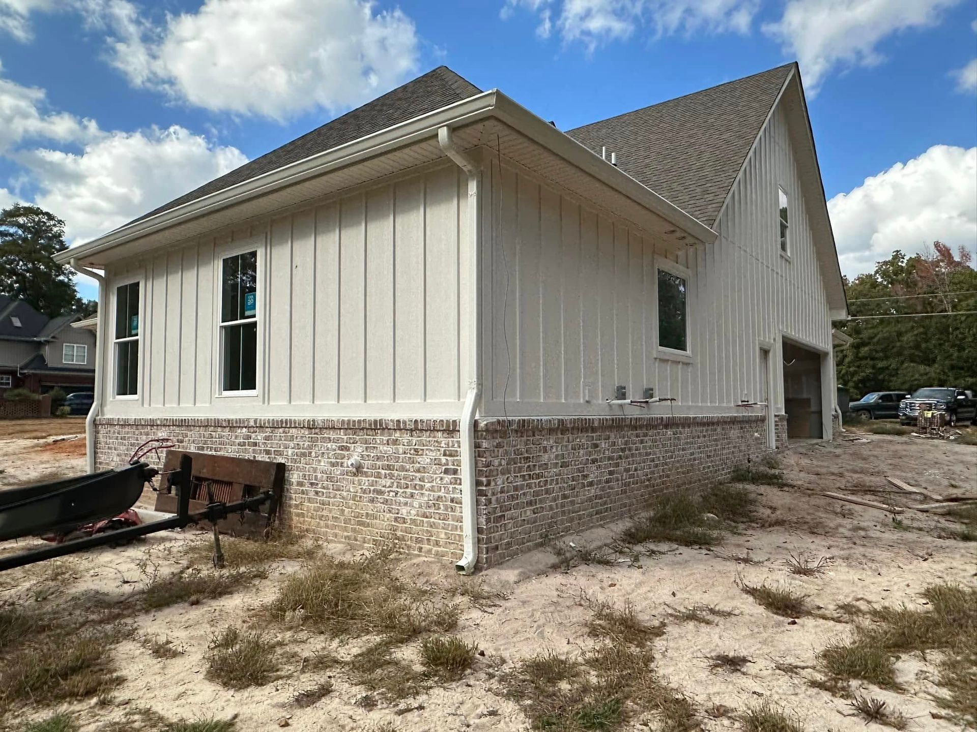 New beige house with stone foundation under construction on a dirt lot, under a cloudy sky
