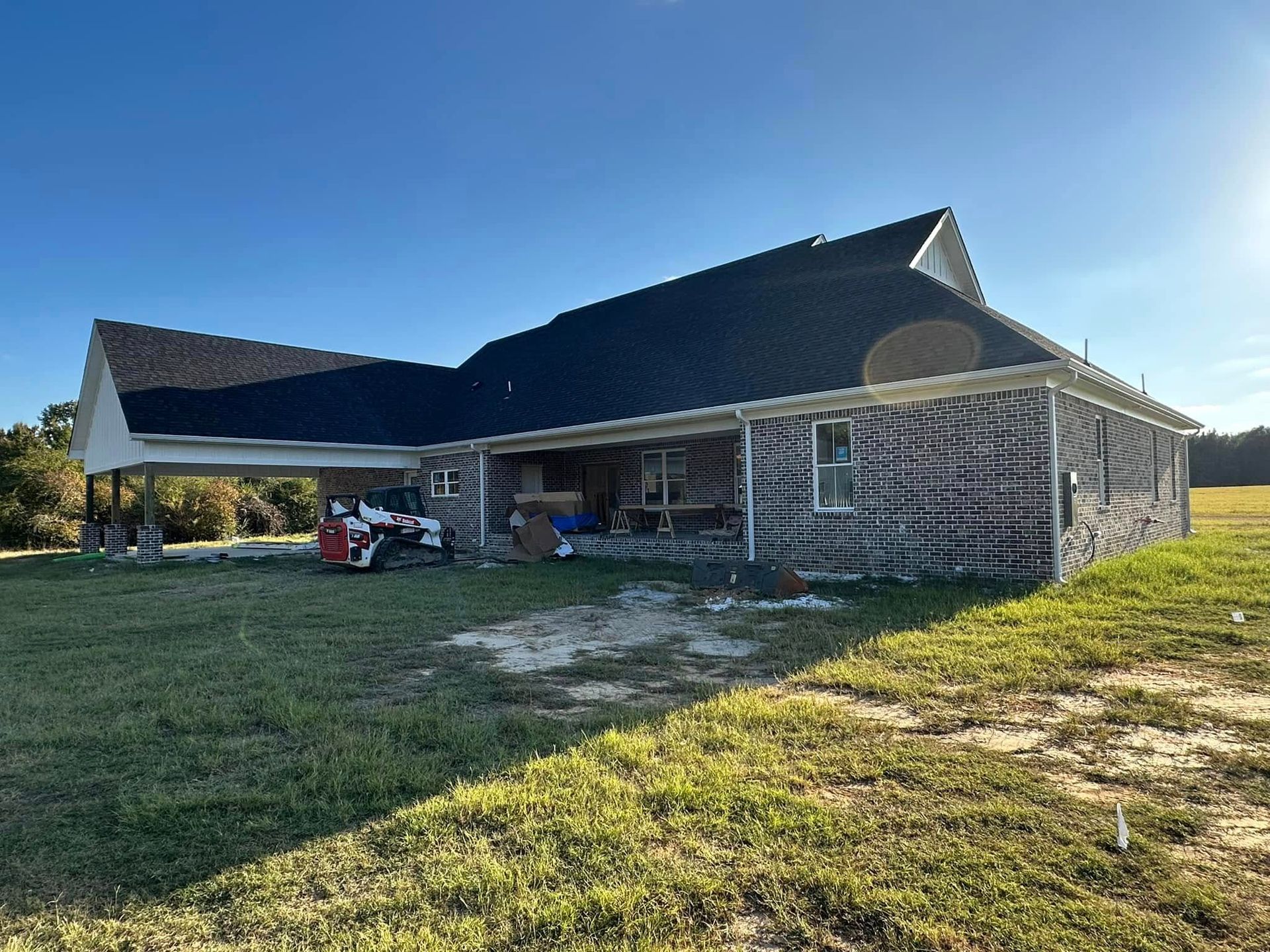 Rural barn-style house with a dark roof and open porch, set on a grassy yard under a clear blue sky.