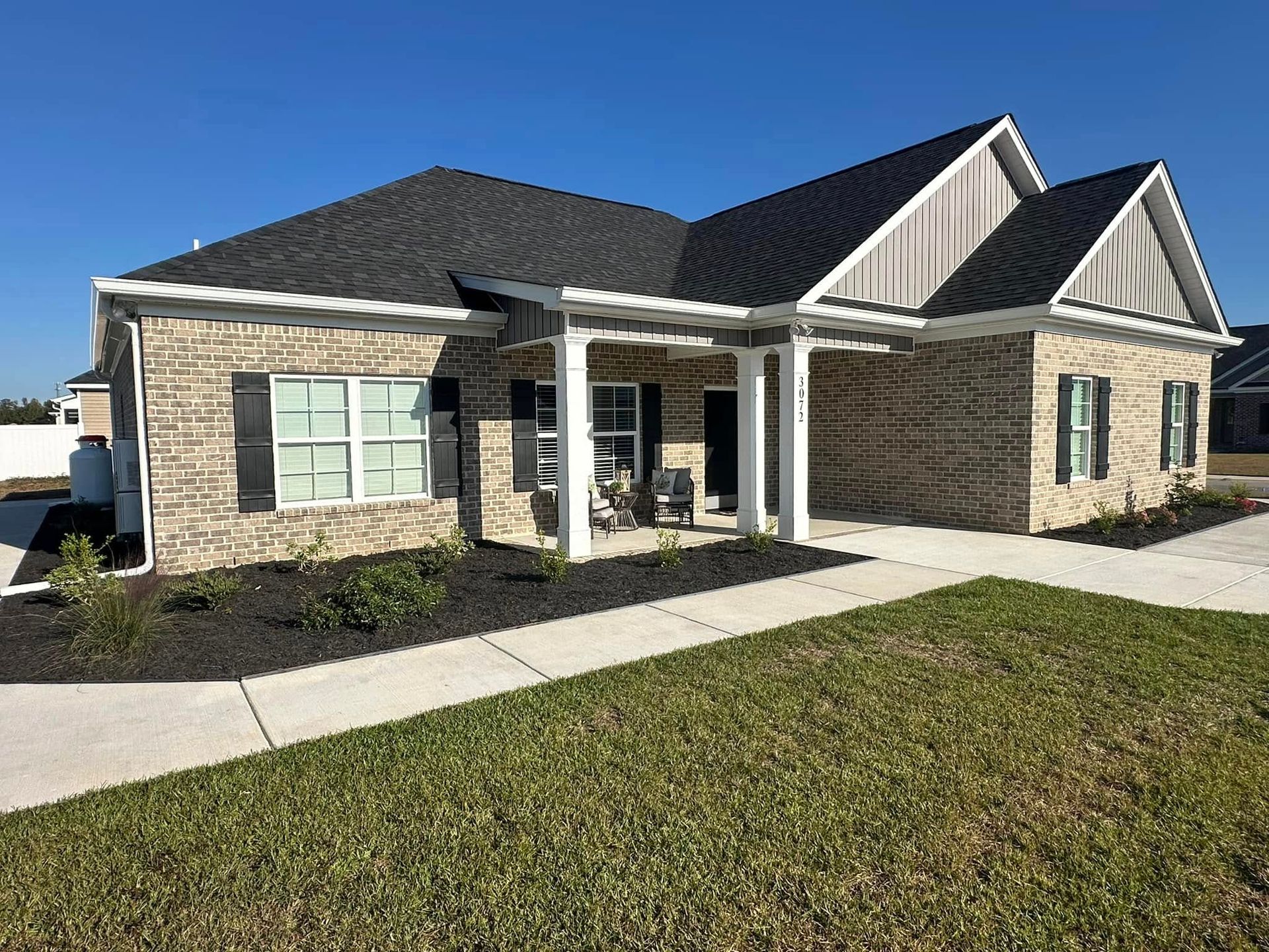 Single-story brick house with dark roof, white trim, and a front porch beside a sidewalk and lawn