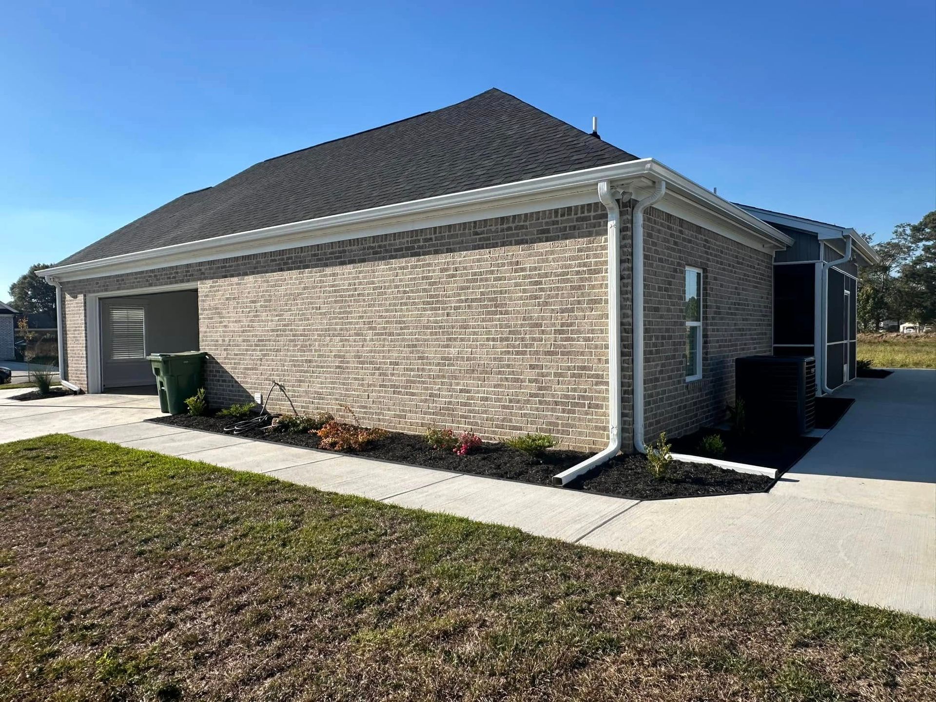 Single-story brick house with a dark roof, driveway, and small front lawn under a clear blue sky