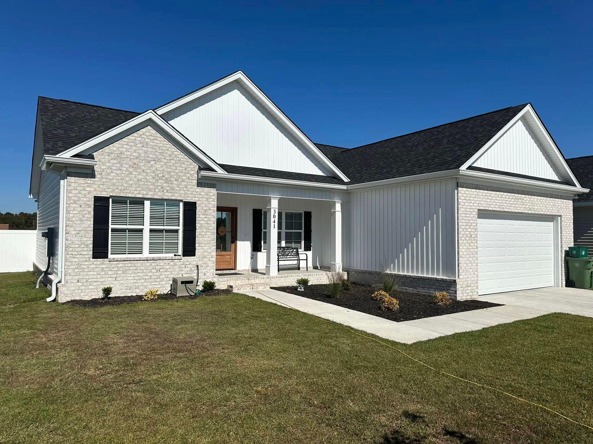 Single-story suburban house with white siding, gray roof, front porch, garage, and a grassy lawn