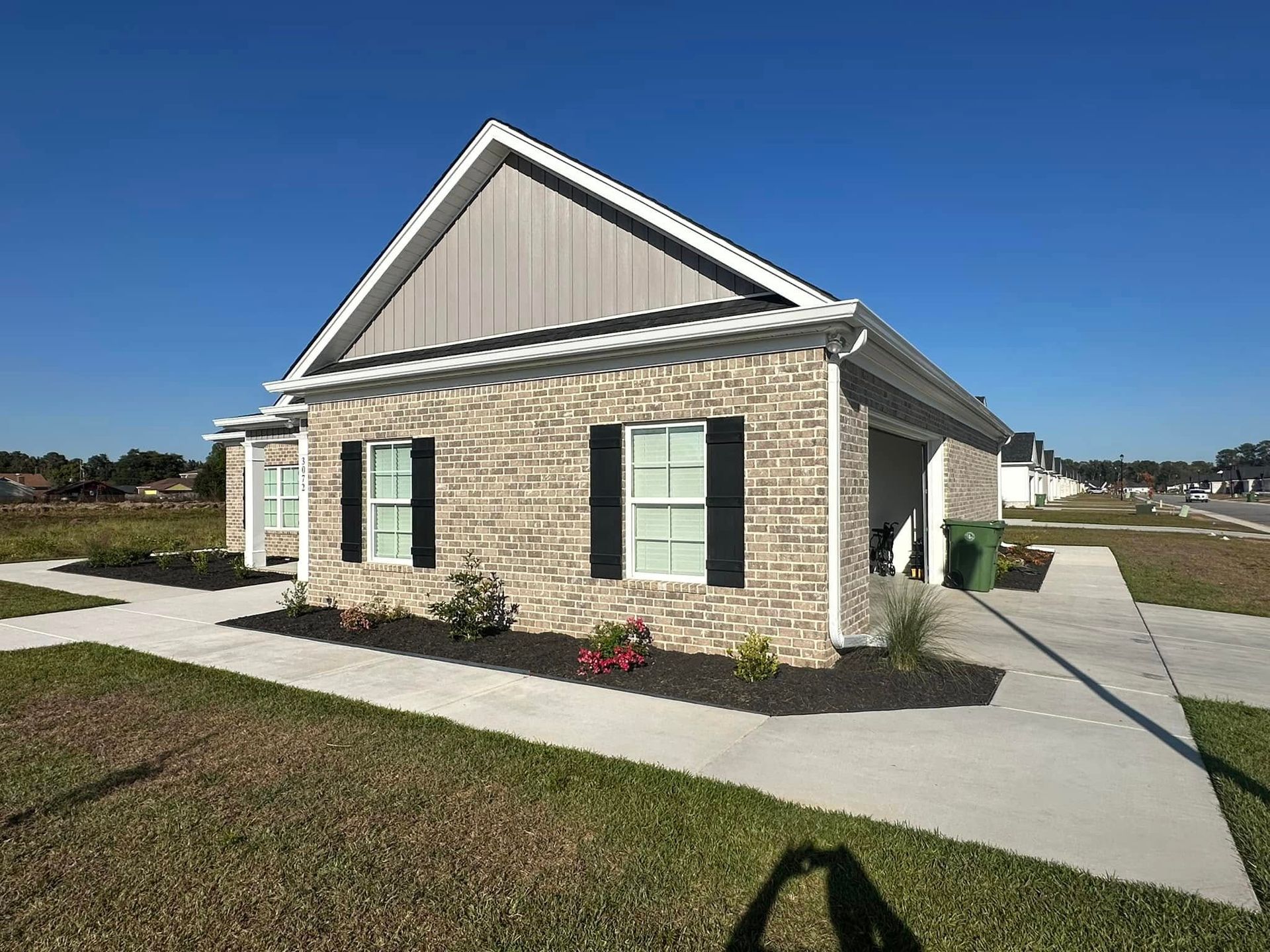 Single-story brick house with green shutters and a concrete sidewalk on a sunny day
