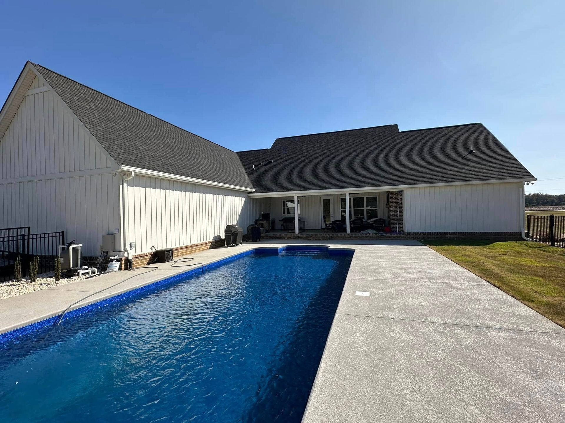 Modern white house with a long blue swimming pool and concrete patio under a clear sky
