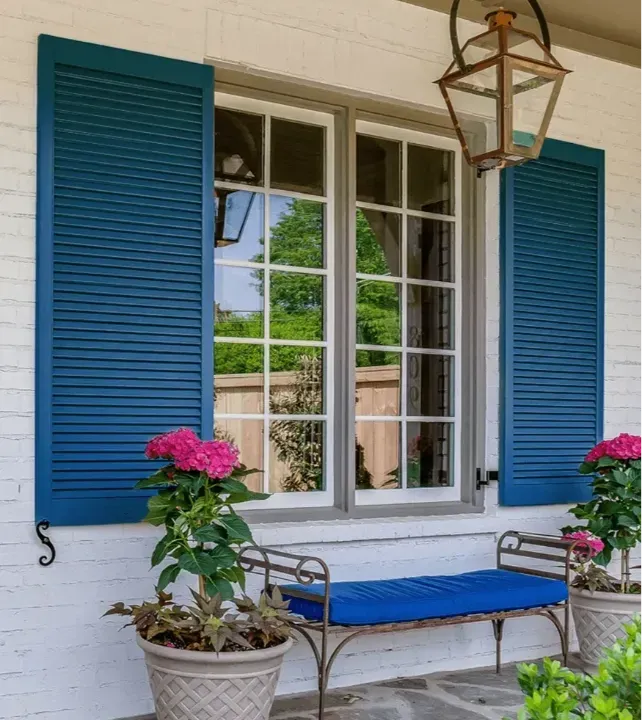 White porch with blue shutters, glass door, bench, and pink flowers in pots