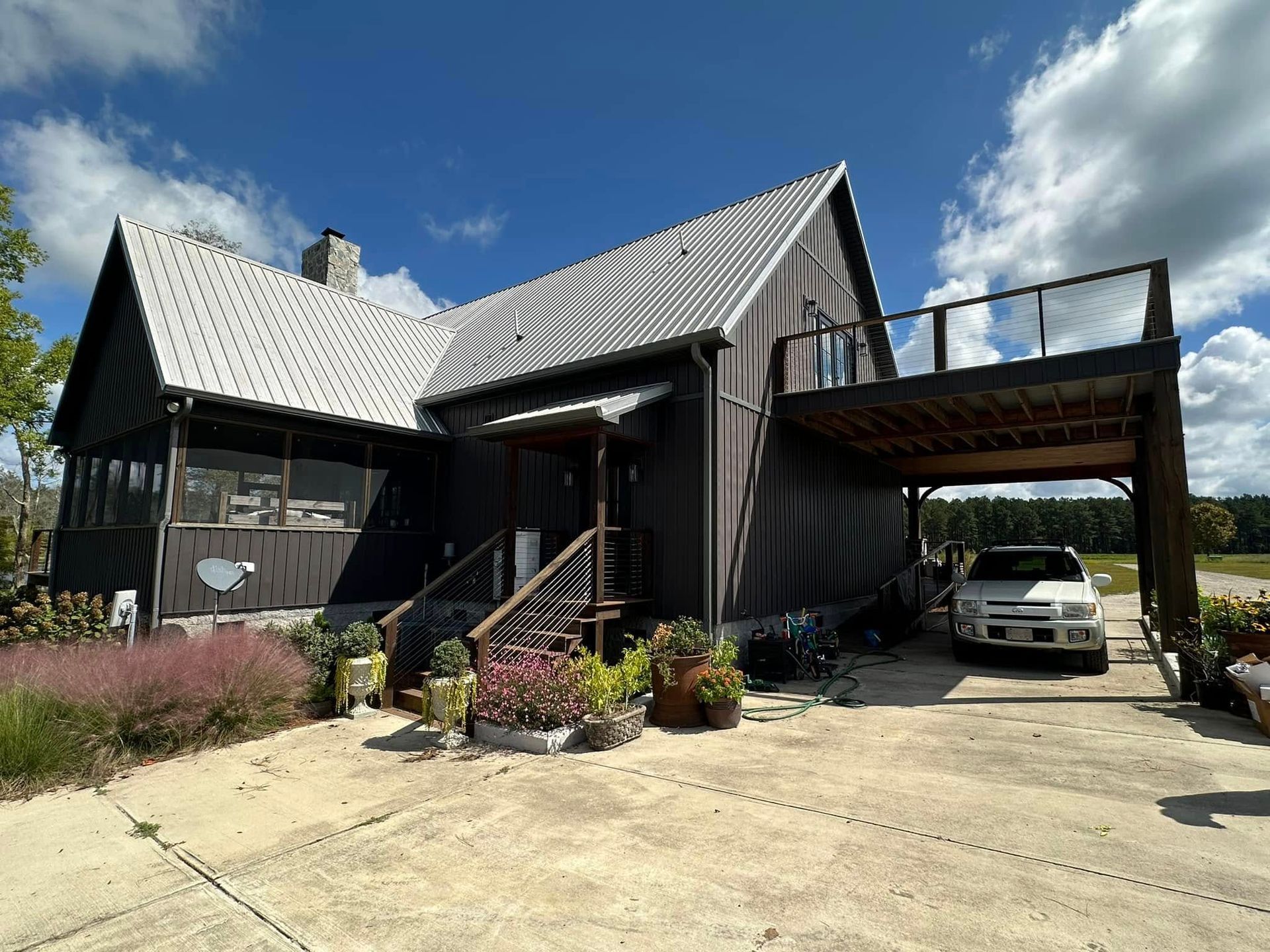 A rustic house with a metal roof, front steps, carport, and a white car parked in the driveway.