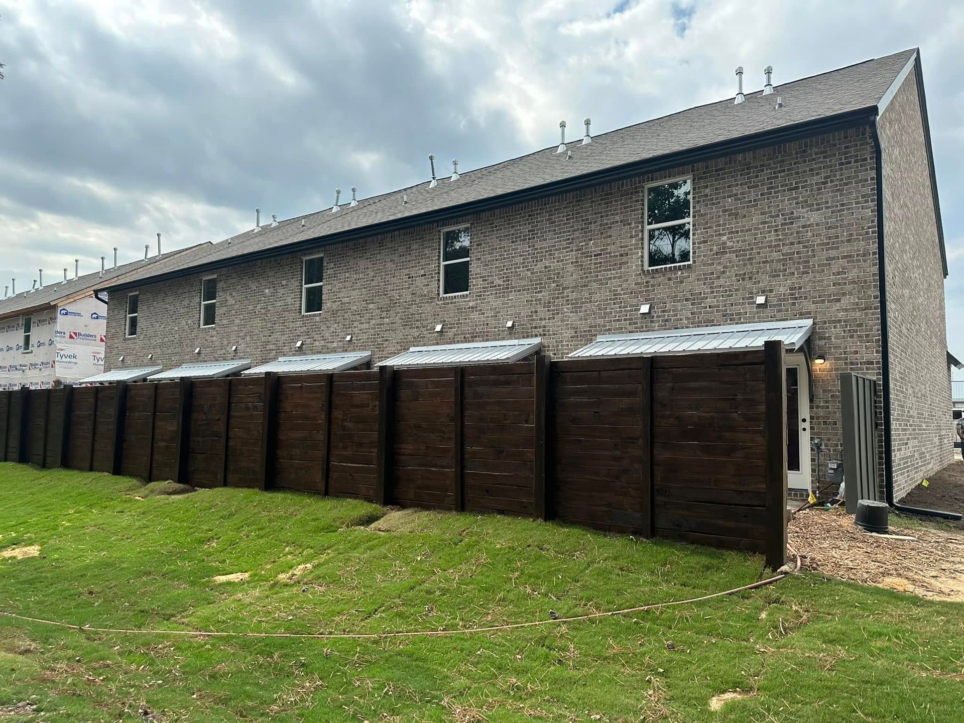 Row of brown wooden sheds beside a long brick building under a cloudy sky