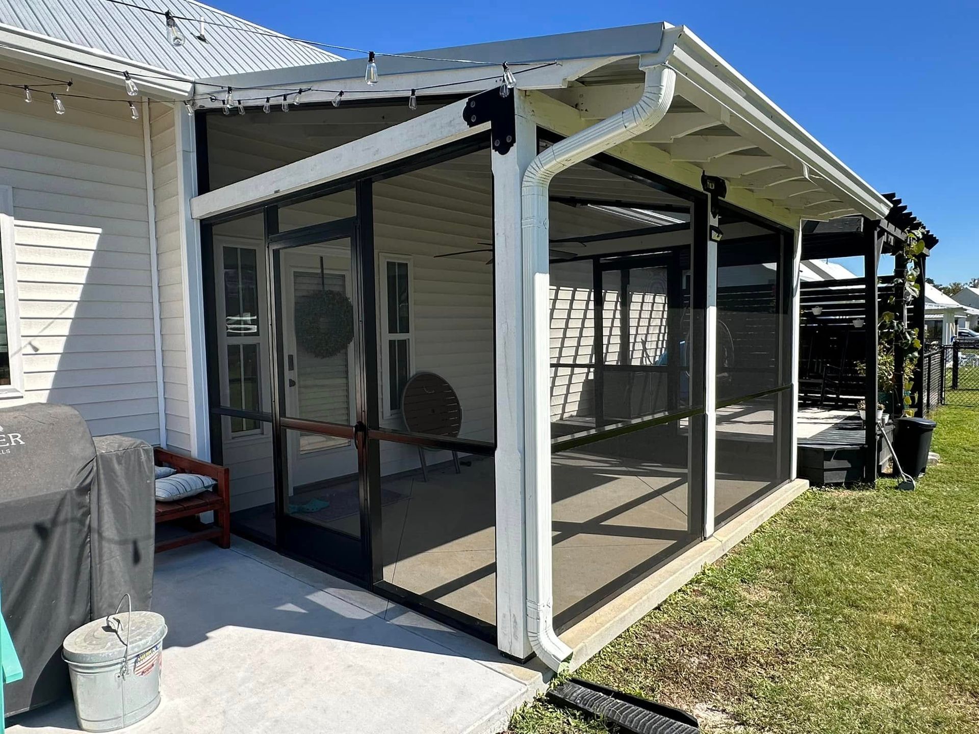 Screened porch with white support posts and mesh panels attached to a house, beside a grassy yard.