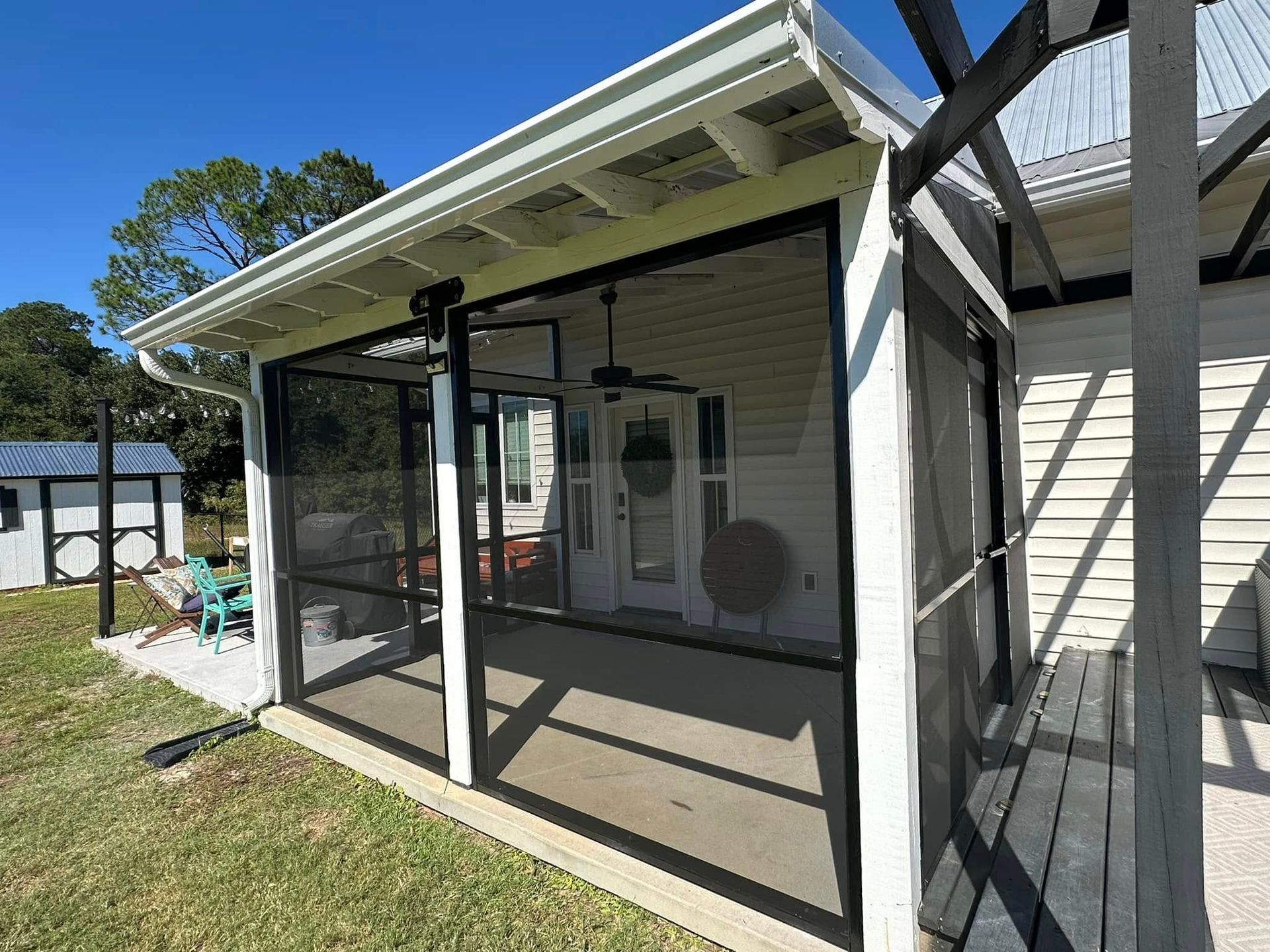 Screened back patio with white siding, black frame screens, and a sloped roof attached to a house