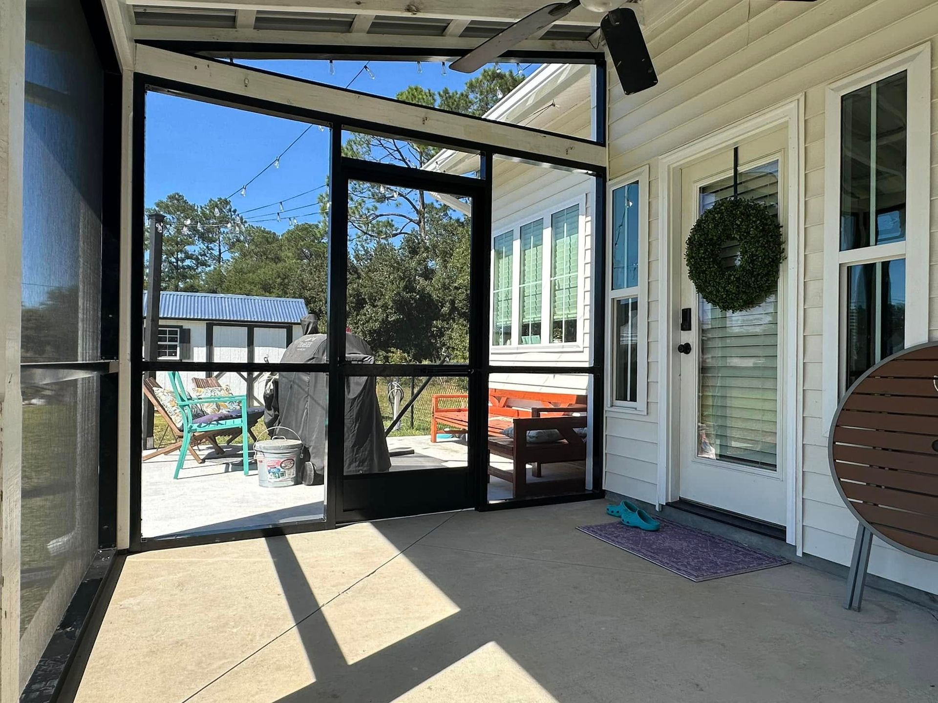 Screened patio with black-framed door, wreath, and wicker chair opening to a sunny backyard.