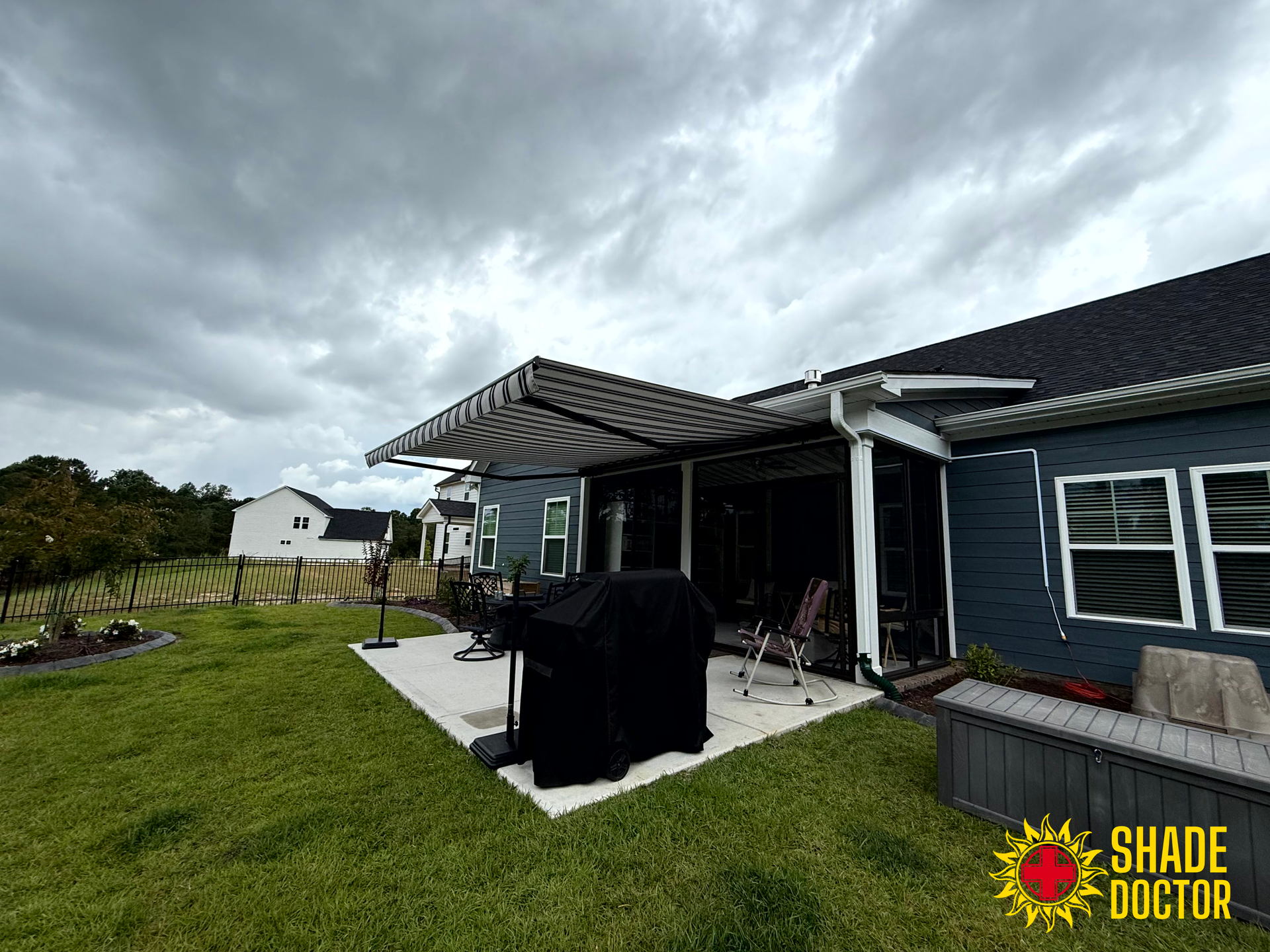 Backyard patio with covered grill, dark house exterior, and cloudy sky
