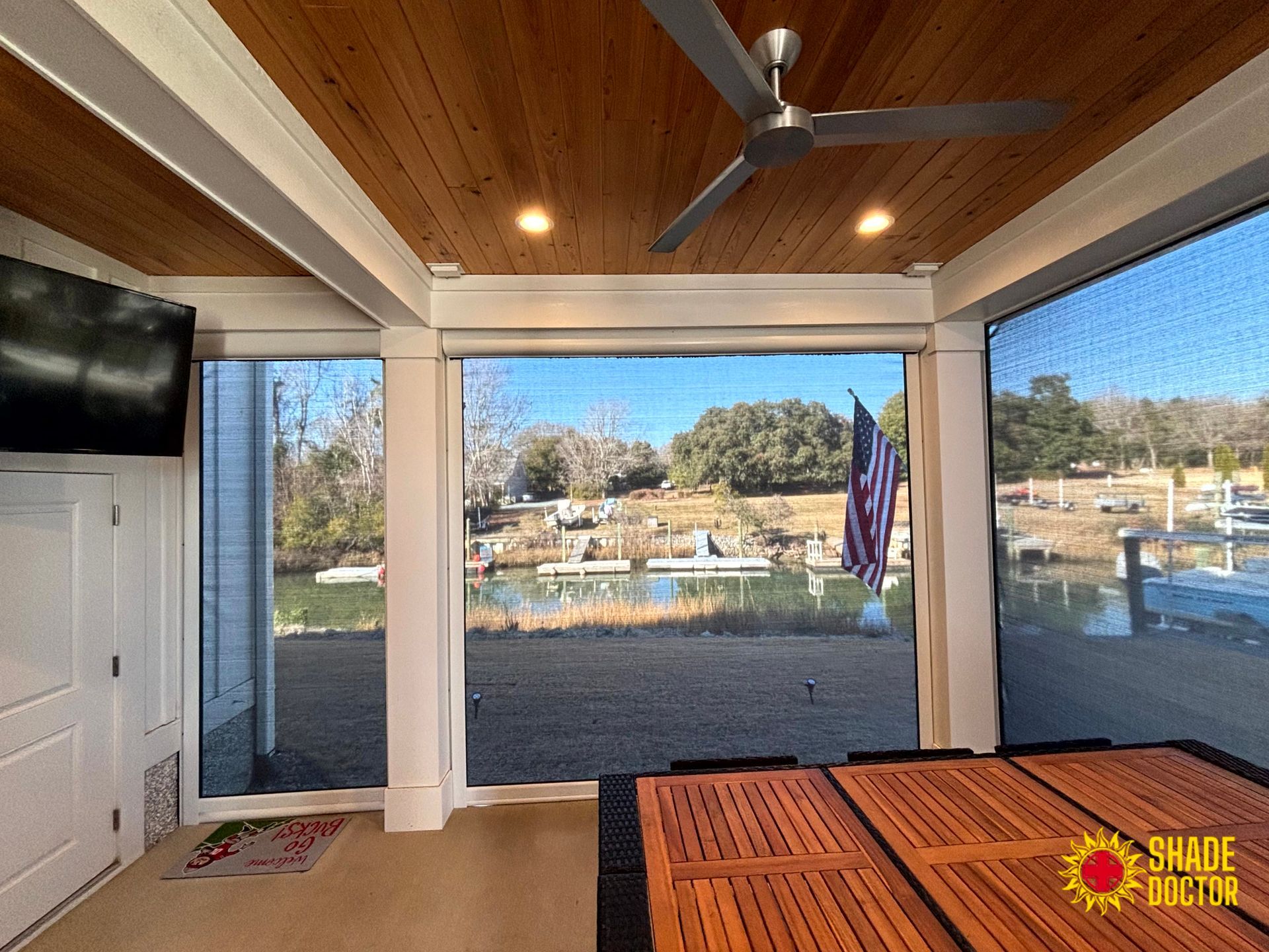 Screened porch with ceiling fan, TV, and view of waterfront and boats beyond the railing