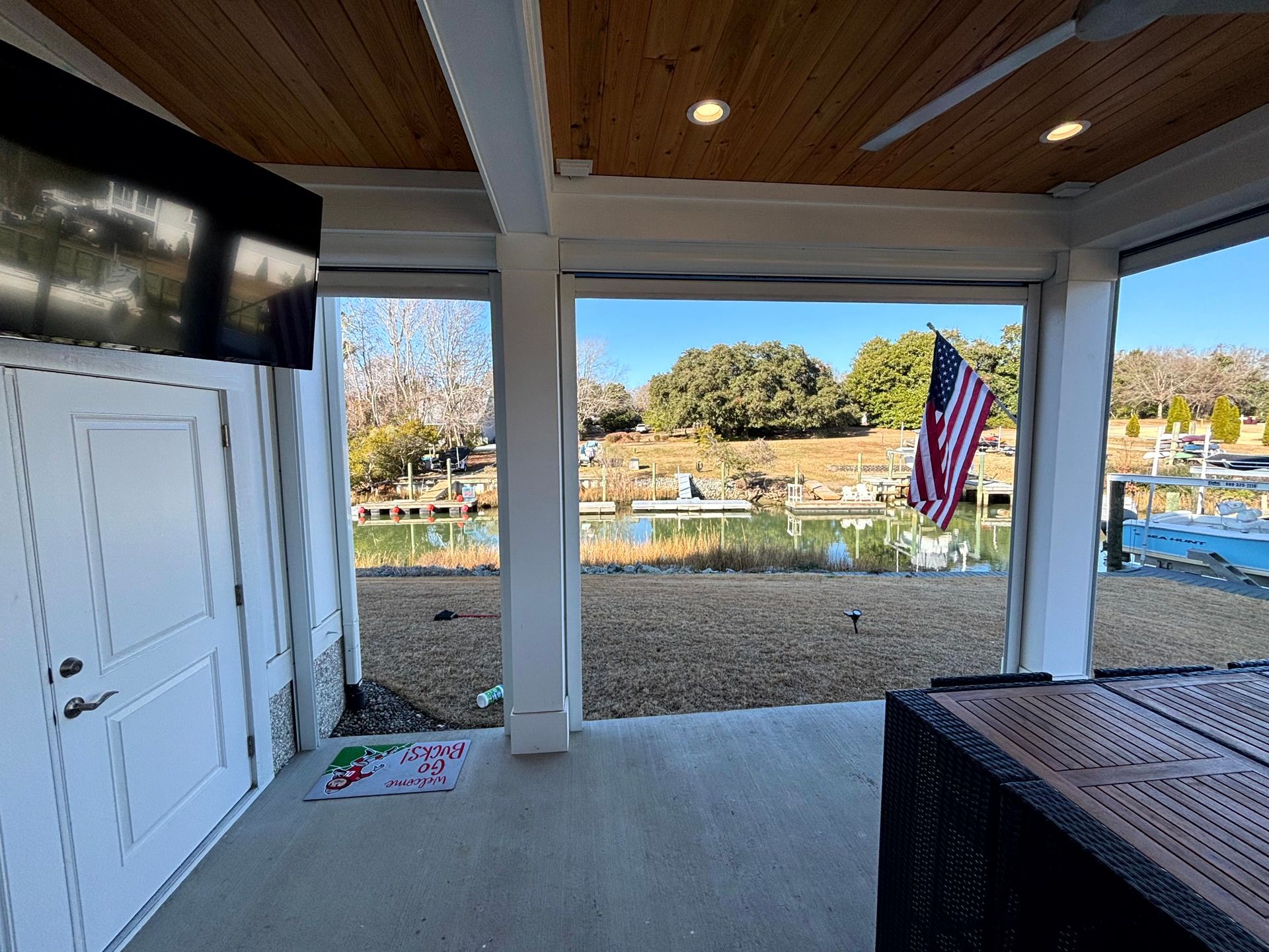 Covered patio overlooking a fenced yard and pond, with an American flag and white storage doors.