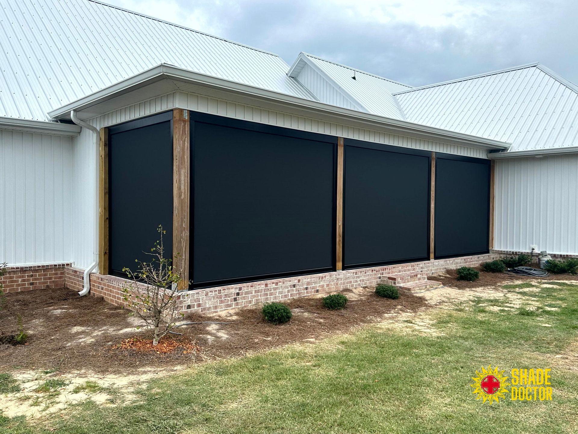 Three dark garage doors on a white shed with a corrugated metal roof and bare yard.