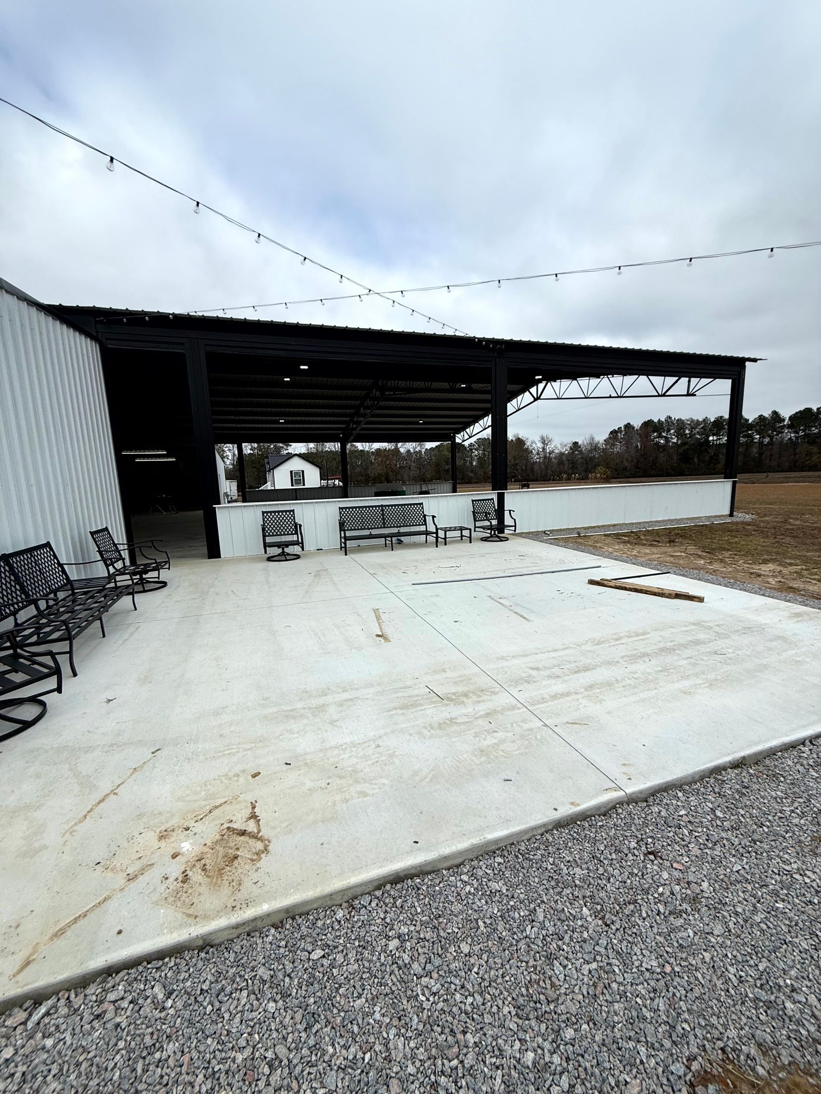 Covered patio with benches, gravel foreground, and string lights under an overcast sky.