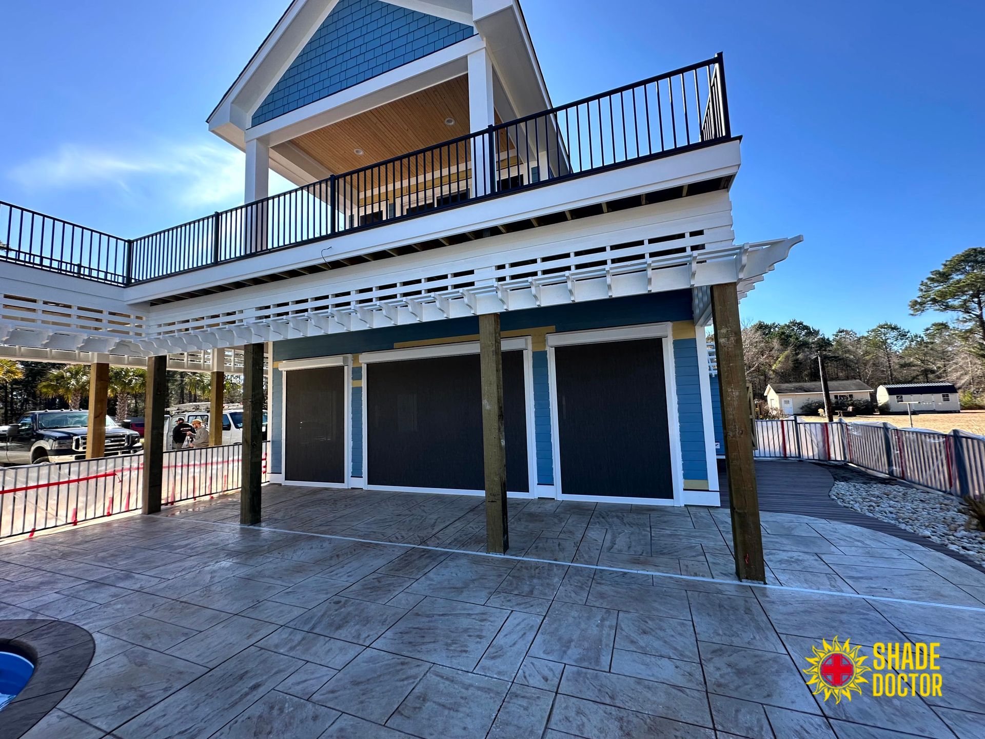 Two-story blue house with upper deck and covered patio on a concrete courtyard