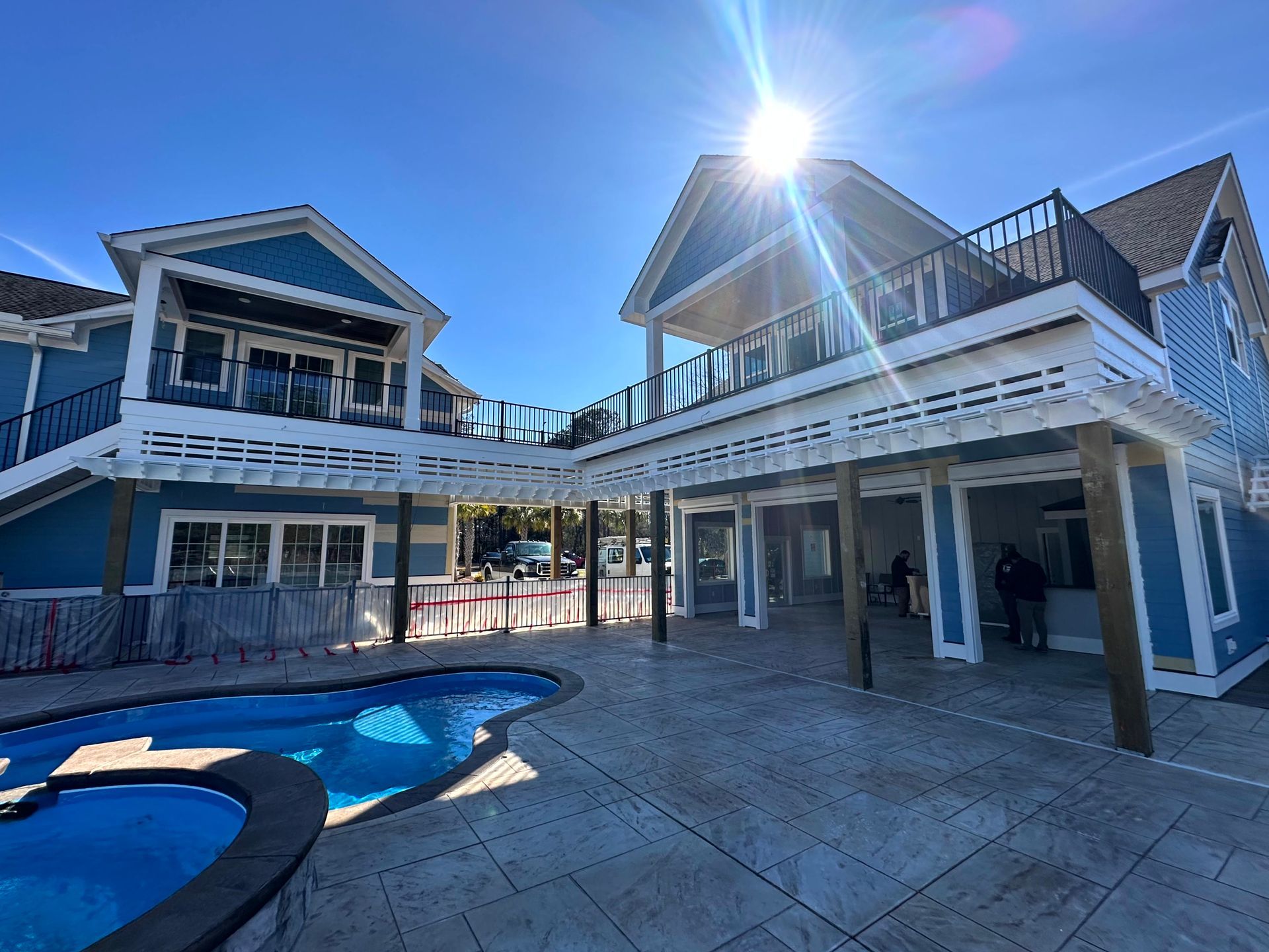 Sunny view of a modern house with a pool, covered patio, and outdoor deck under a bright blue sky