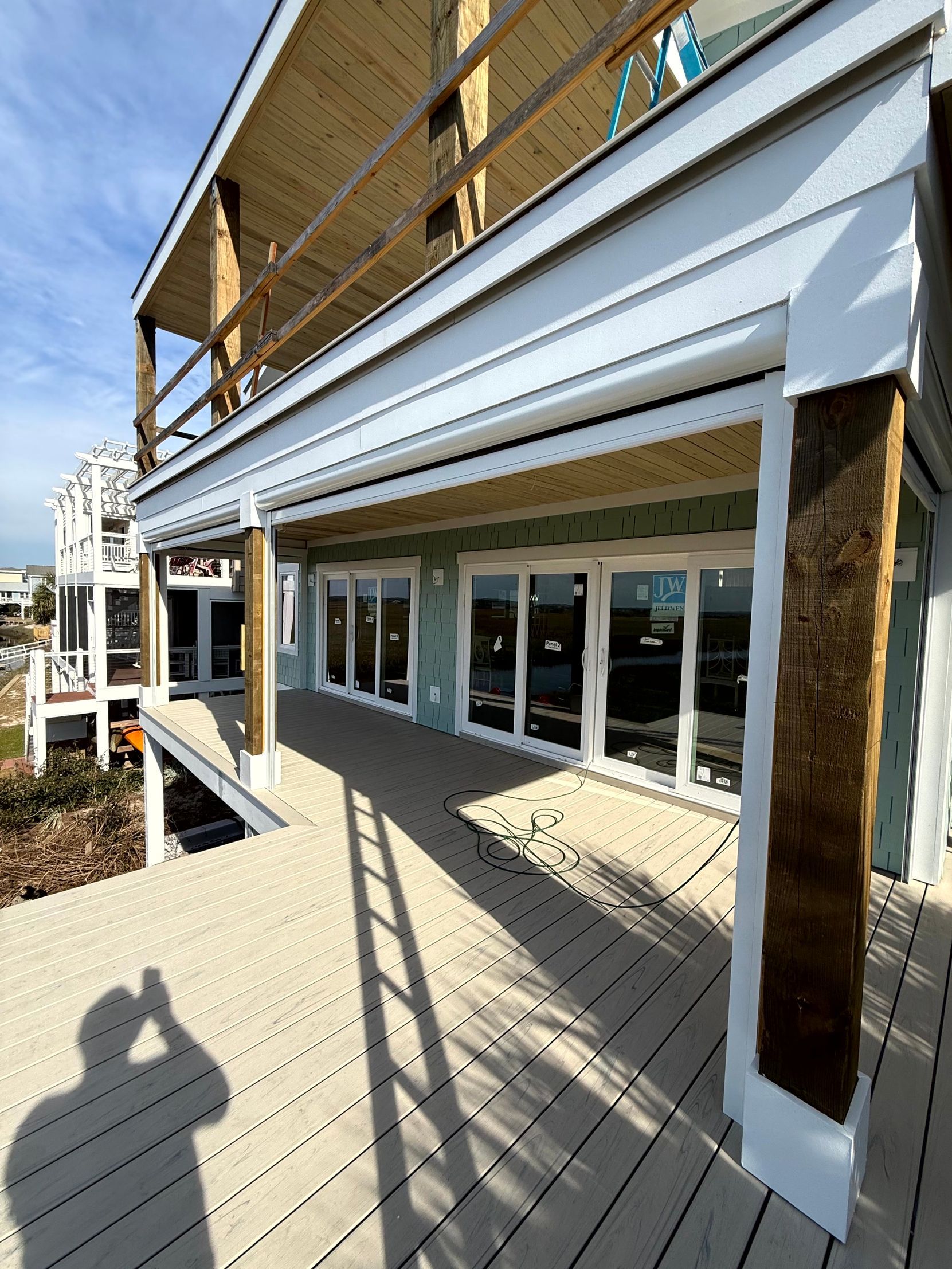 Covered building walkway with white awnings and glass doors, viewed from a wooden deck in bright sunlight