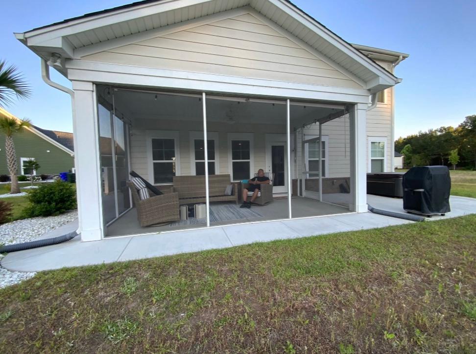 Covered backyard patio with white screened porch, wicker furniture, and a grill next to a house