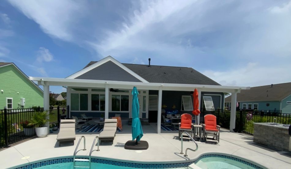 Poolside patio with white pavilion, lounge chairs, turquoise umbrellas, and a pool in front of a house