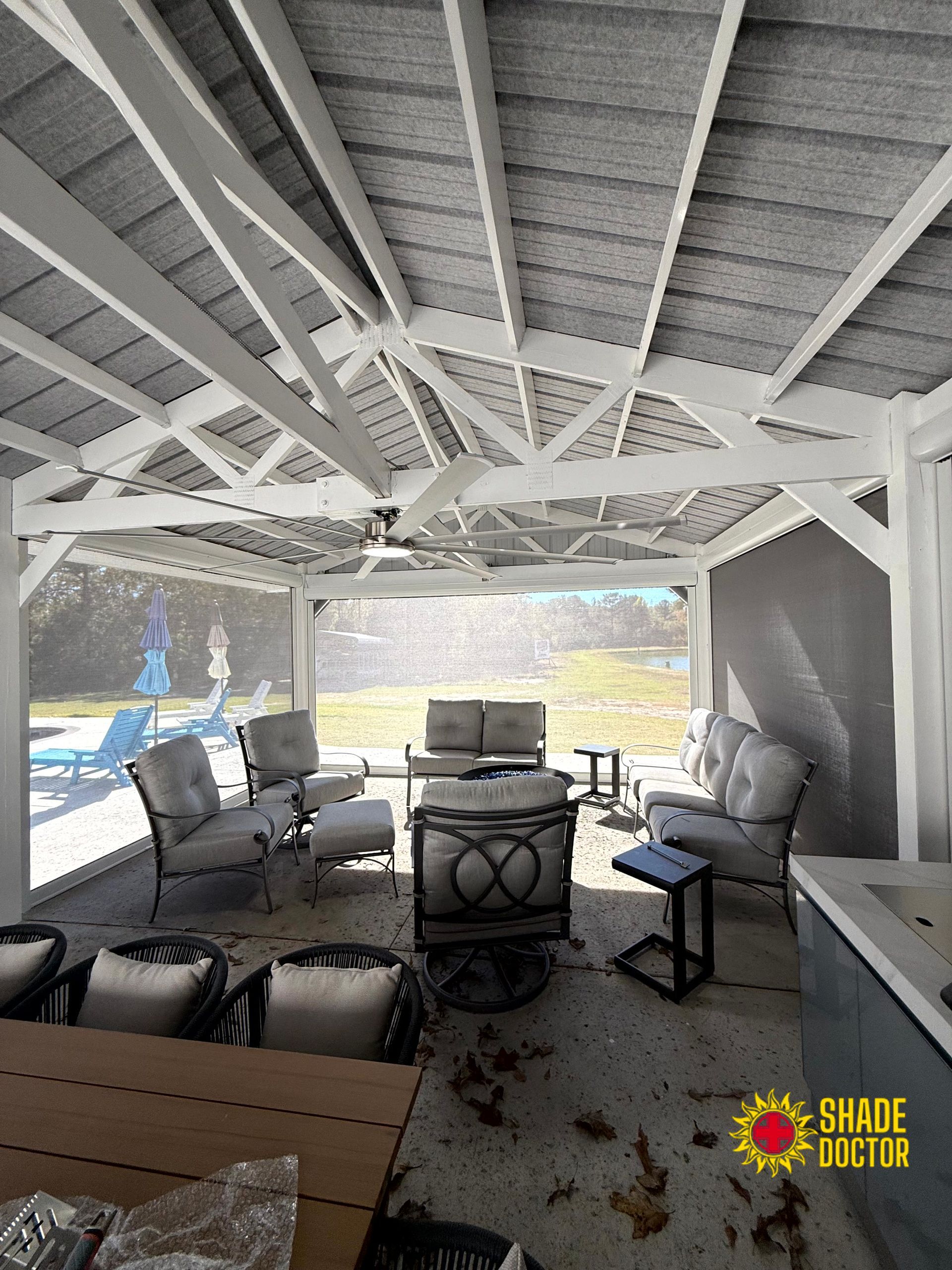 Covered patio with white beams, wicker chairs, and a TV overlooking a bright outdoor view.
