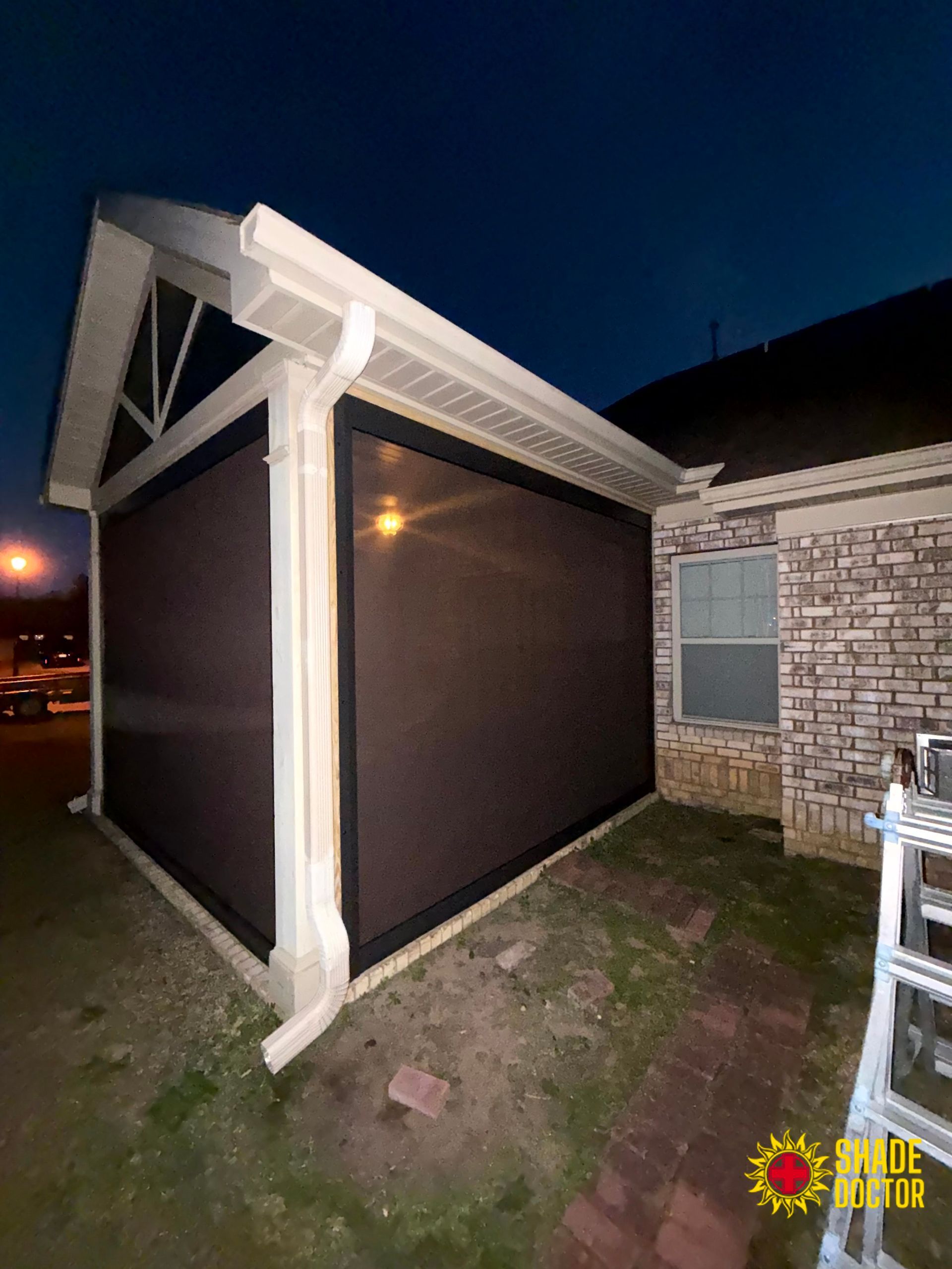Side view of a house patio enclosure with dark screen panels and white trim at dusk