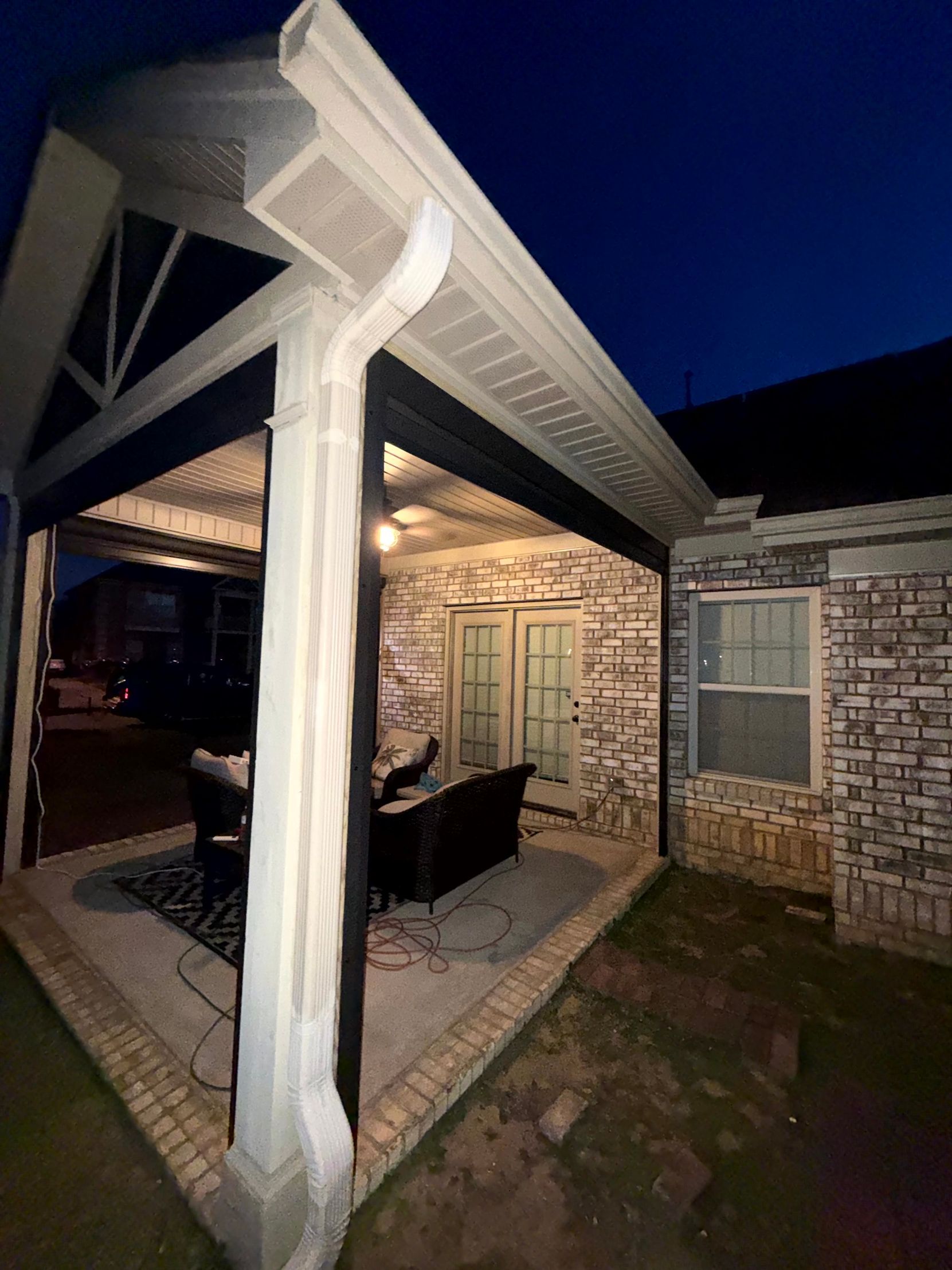 Covered brick patio at night with lit ceiling, white column, and outdoor dining furniture.