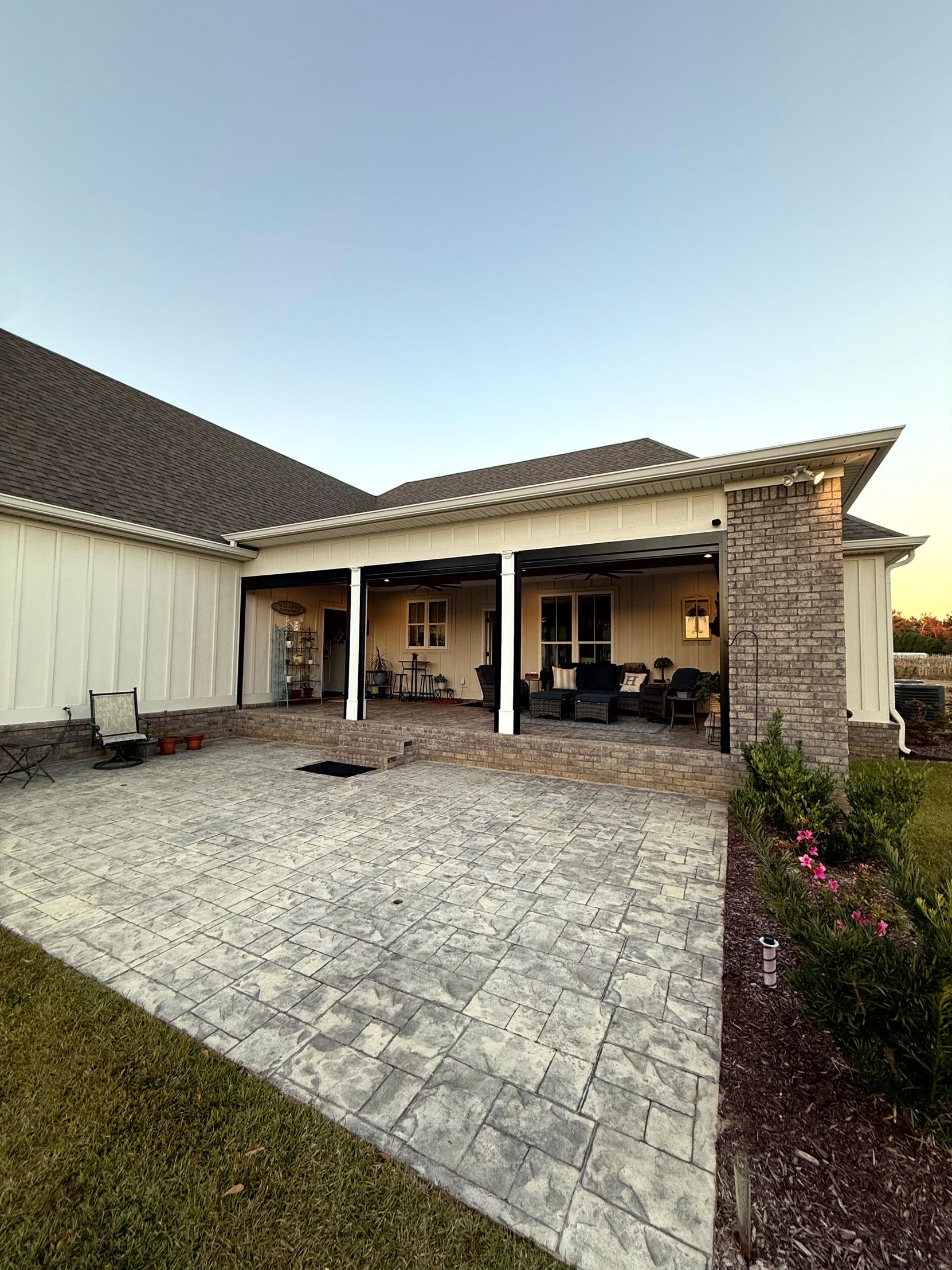 Covered patio with outdoor furniture beside a gravel driveway and landscaped yard at a house