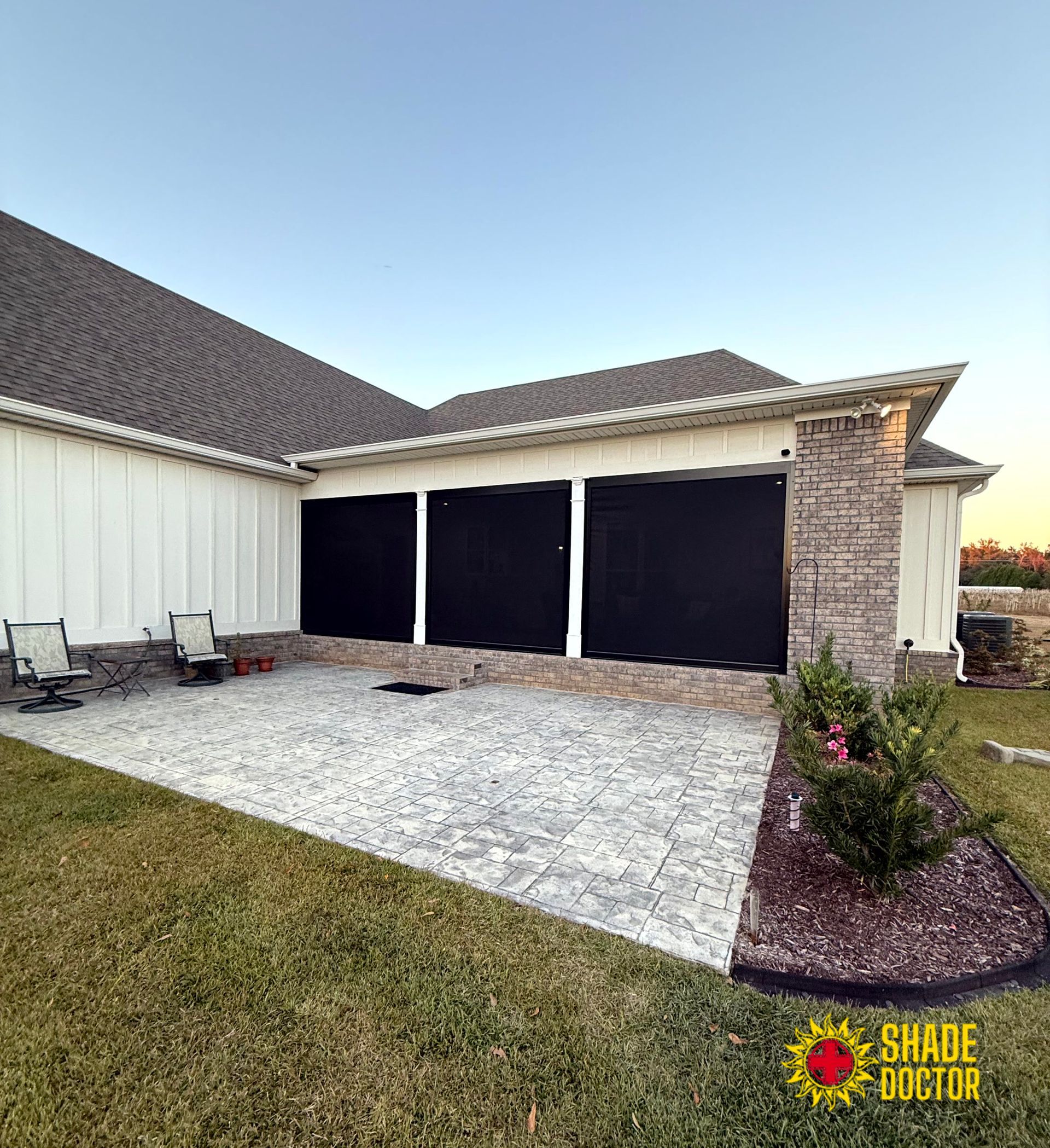 Suburban house exterior with three black garage doors, gravel driveway, and small front landscaping.