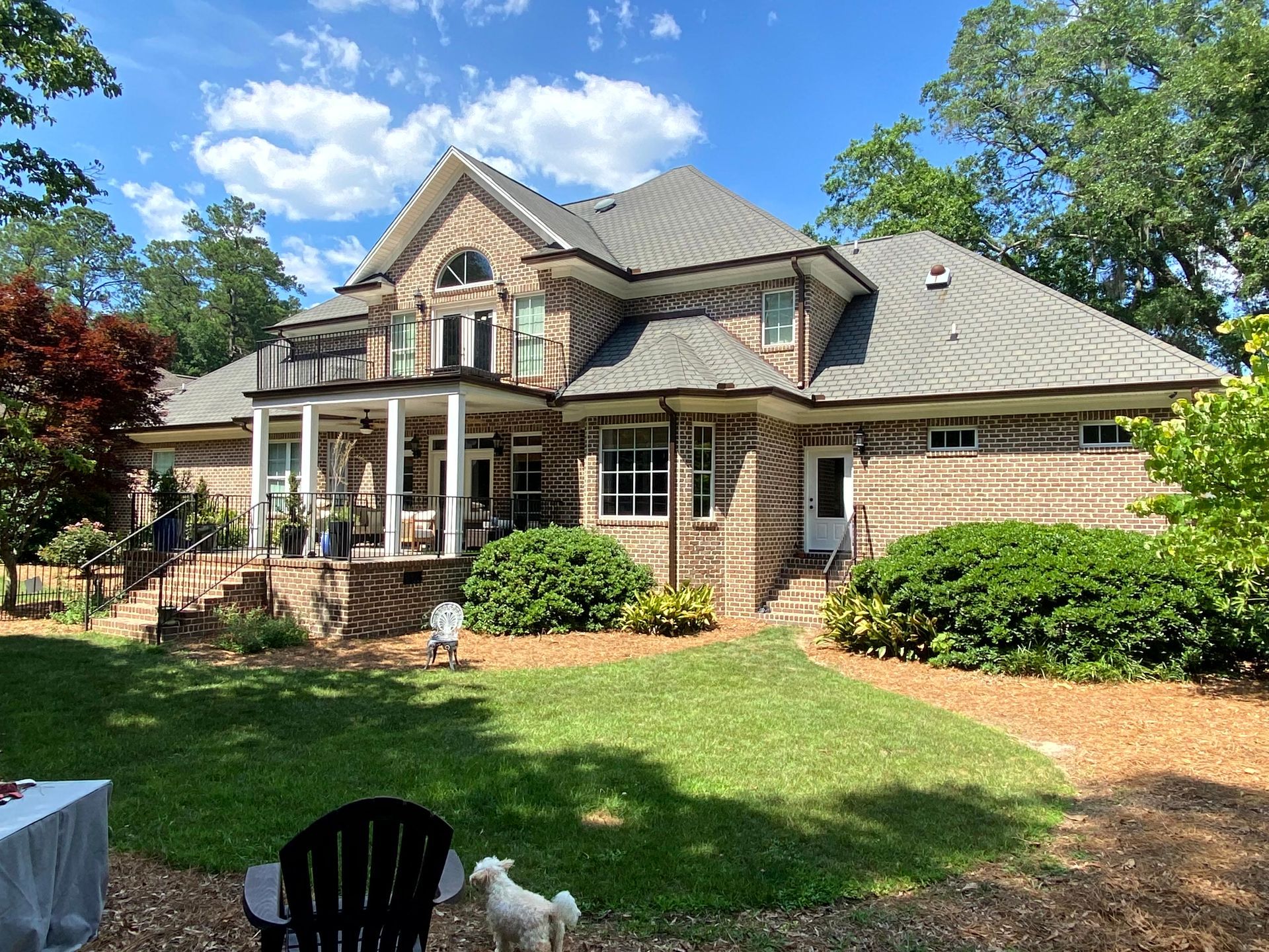 Large brick house with a covered porch, green lawn, and blue sky on a sunny day