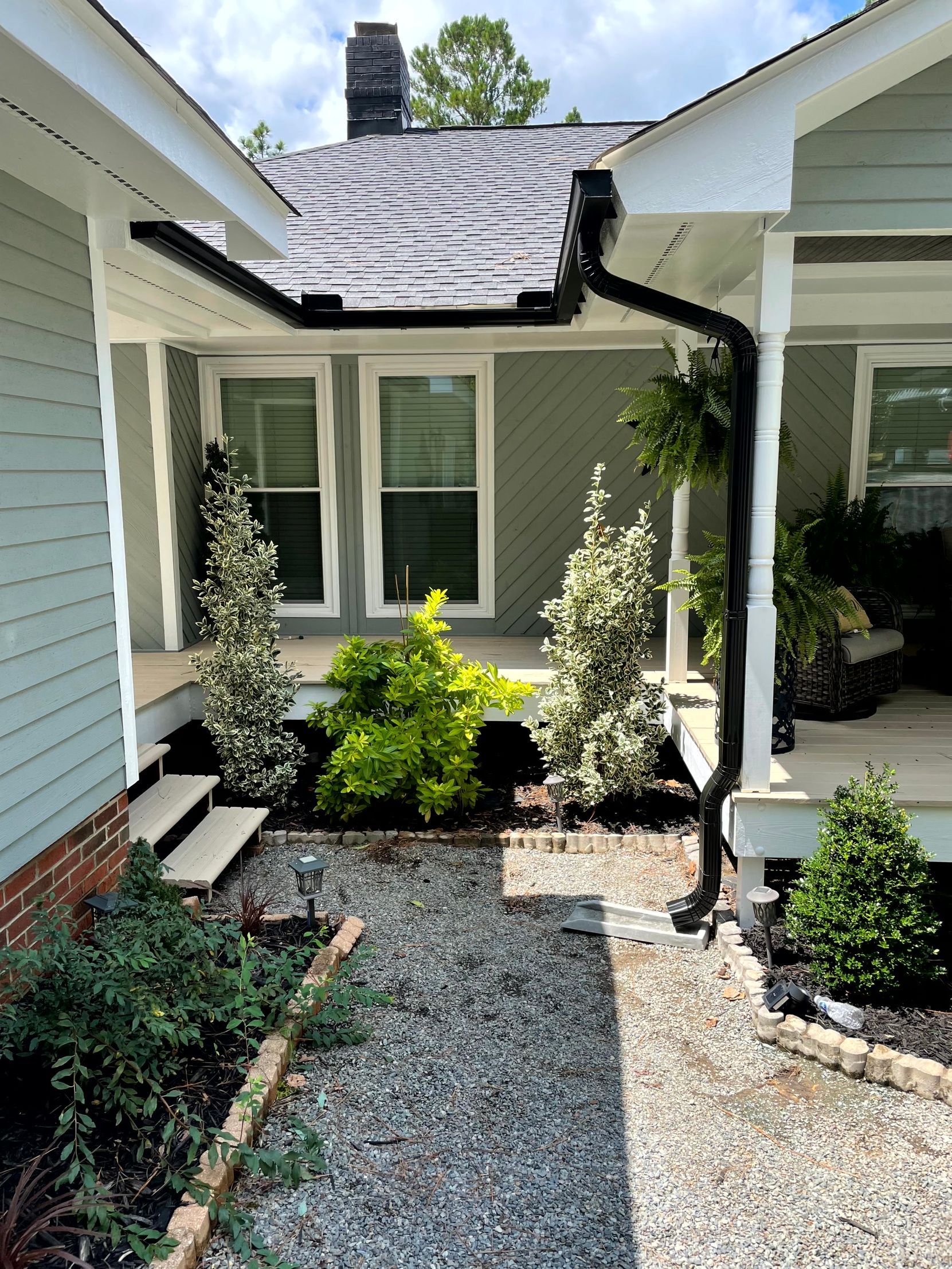 Front entry courtyard with gravel path, white siding, potted greenery, and damaged roof over the doorway.