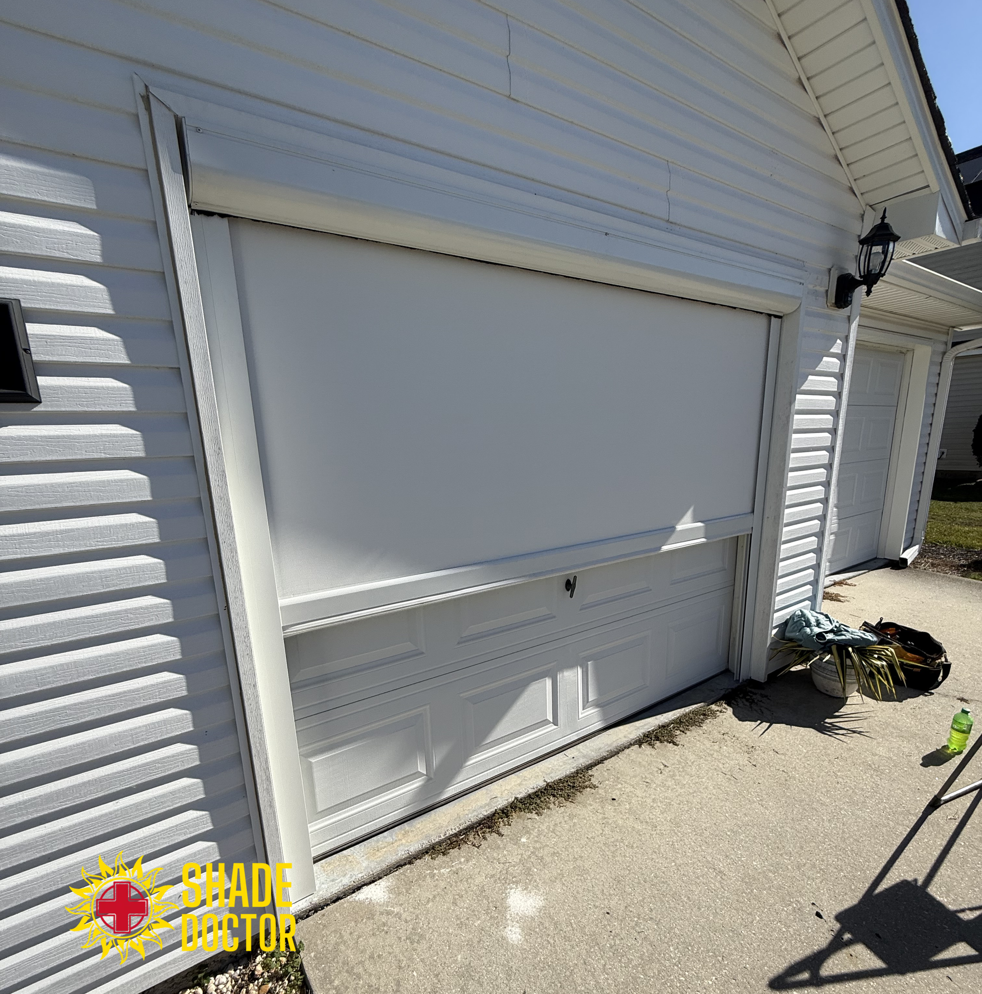 Closed white roll-up garage door on a white house exterior in bright sunlight.