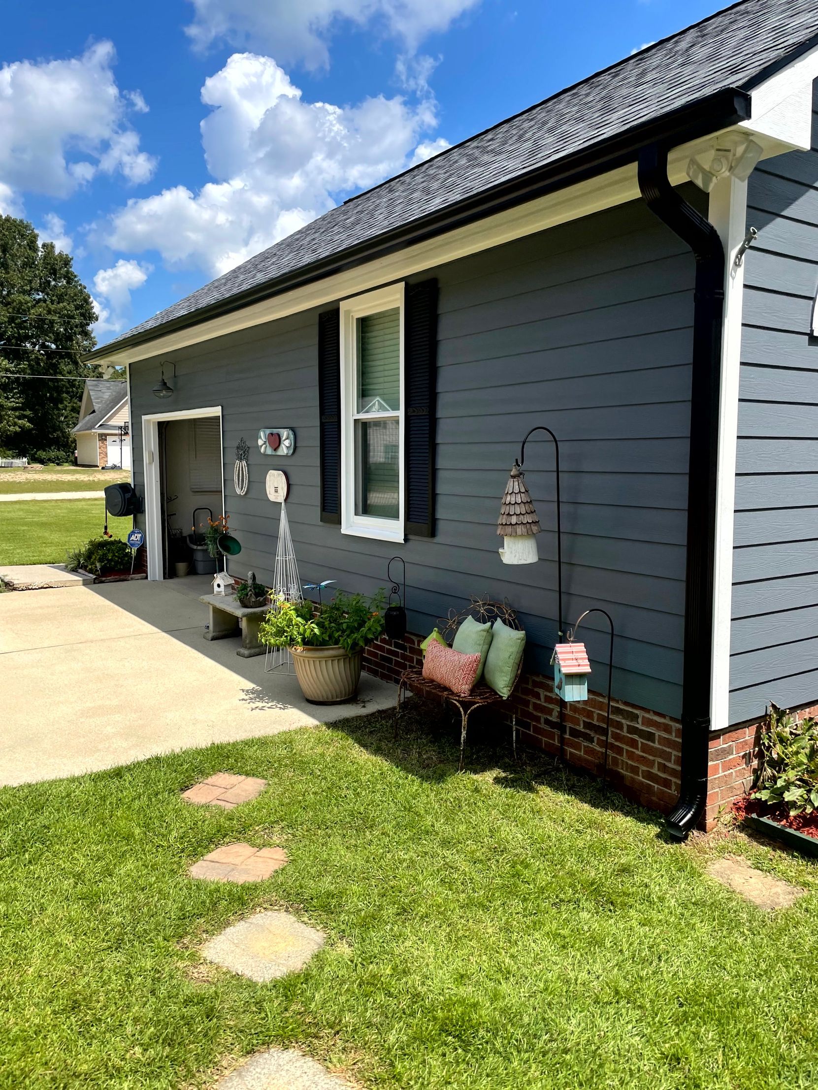 Suburban house exterior with gray siding, flower pots, and stepping stones along the lawn