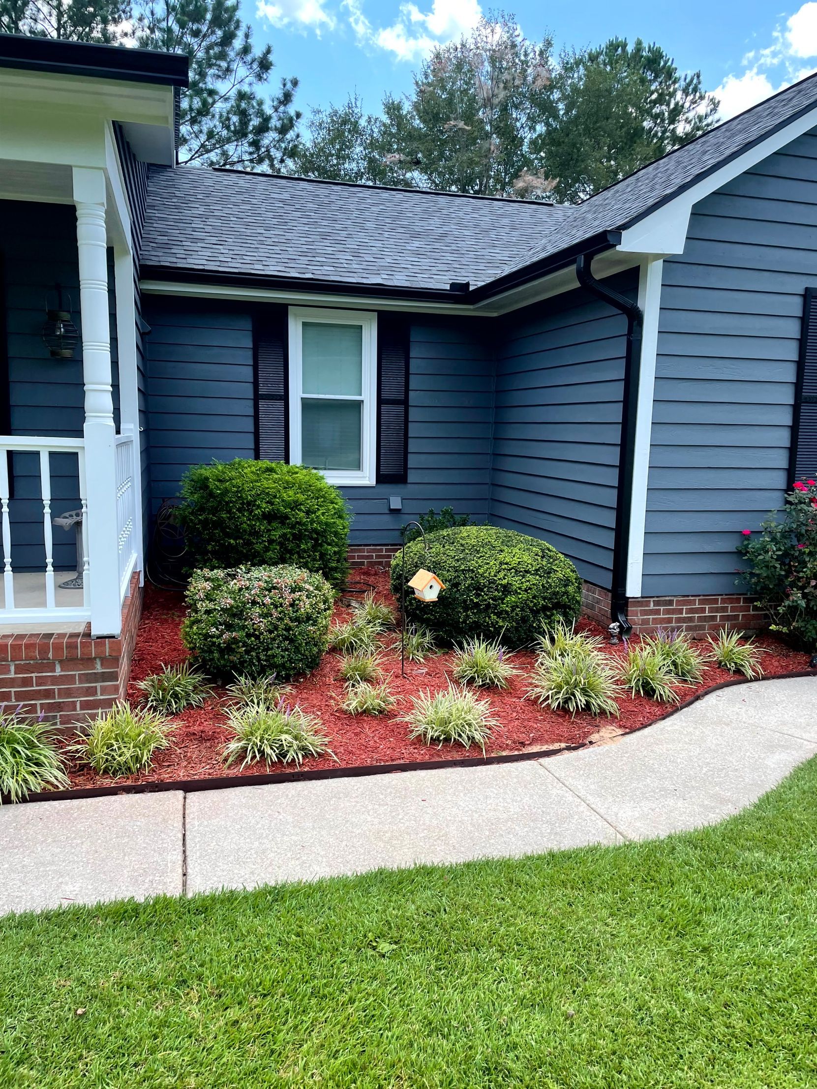 Blue house exterior with white trim, front porch, curved walkway, and landscaped flower bed.