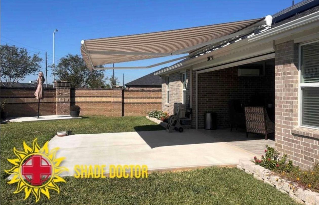 Backyard patio with tan retractable awning, brick house, and lawn under a blue sky.